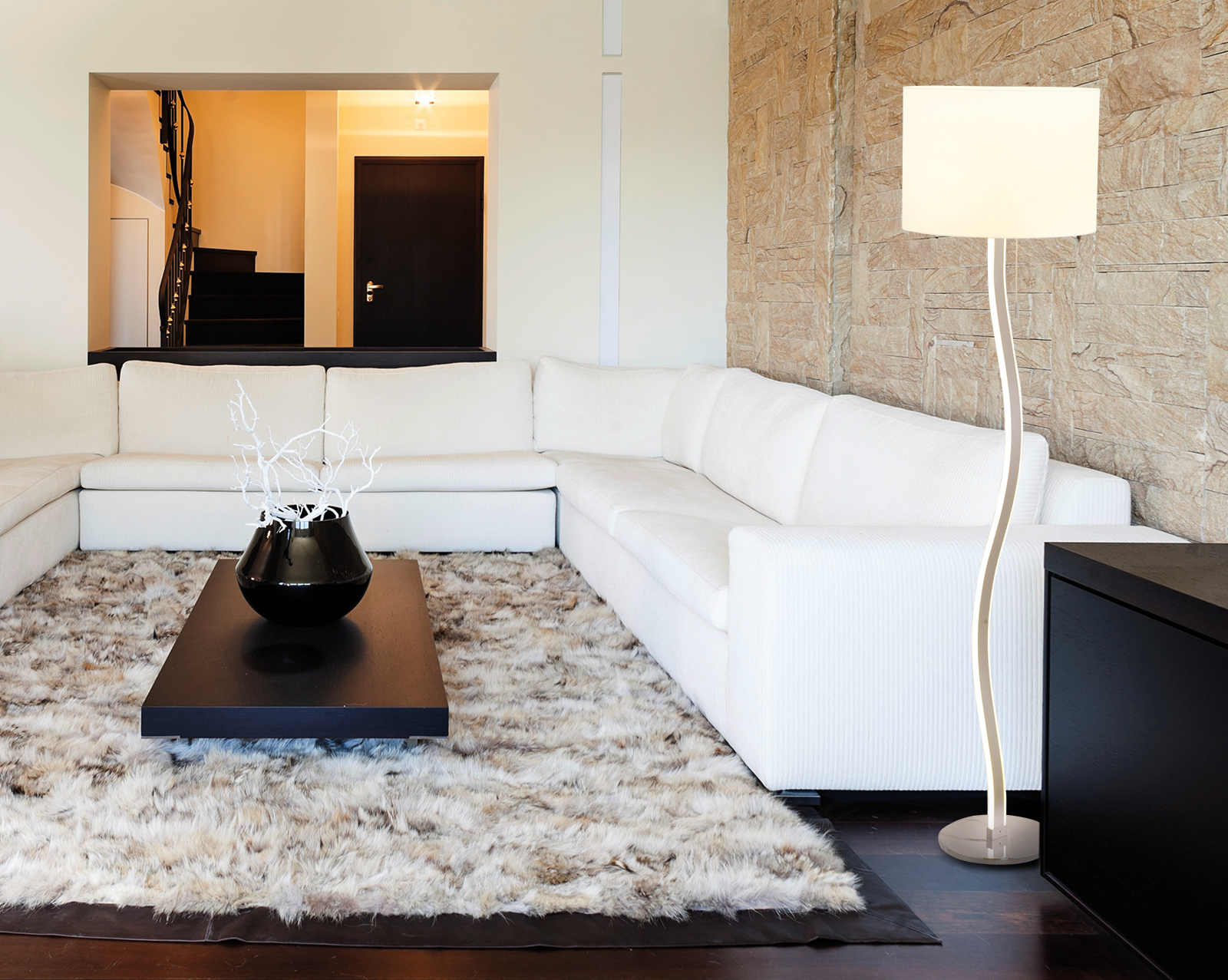 Modernes Wohnzimmer mit weißem Sofa, schwarzem Tisch, hoher Lampe und Steinwand.