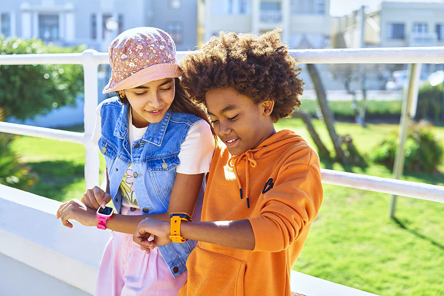 Due bambini che guardano smartwatch. Una ragazza indossa un orologio rosa, un ragazzo uno arancione.