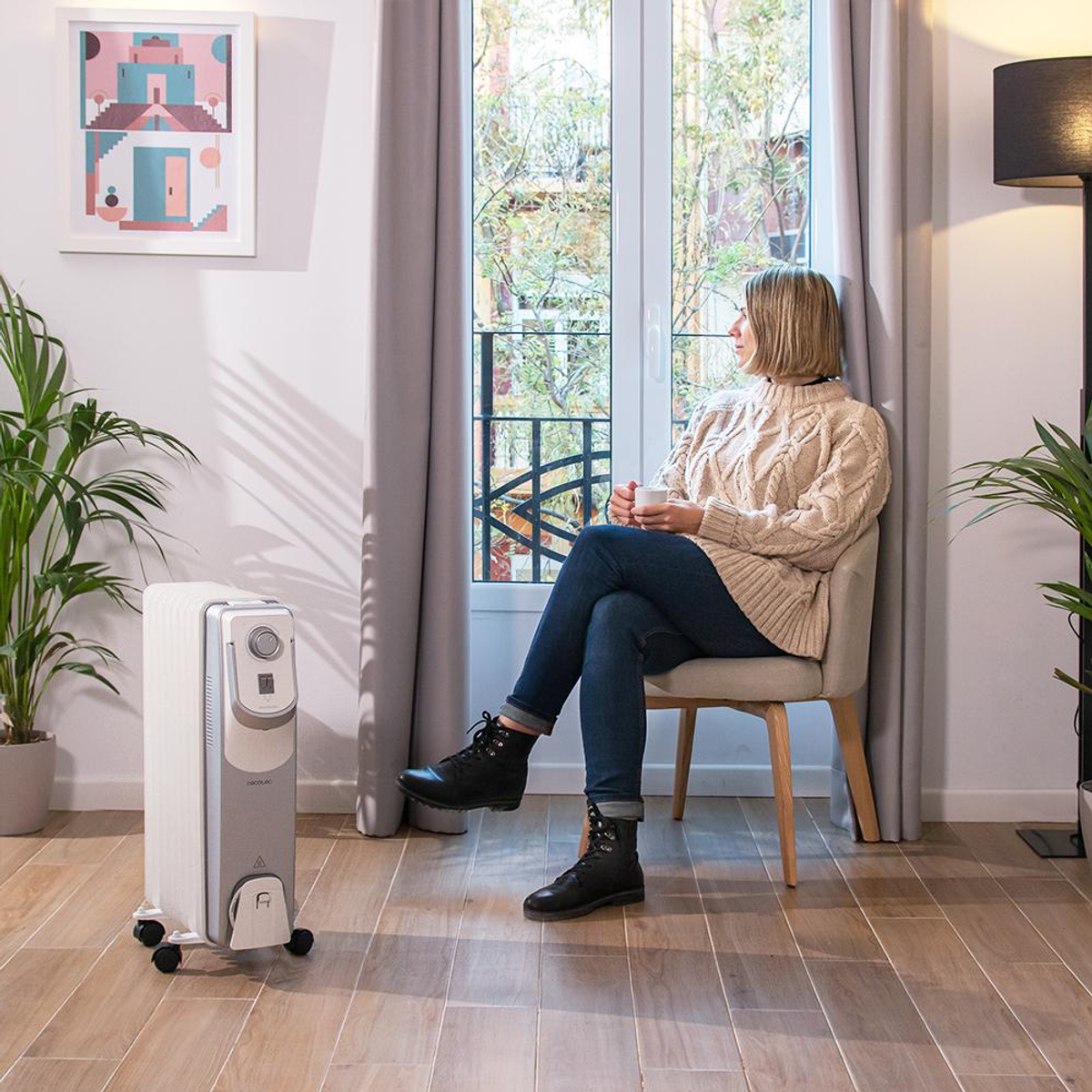 Kobieta siedząca obok grzejnika, patrząca przez okno.