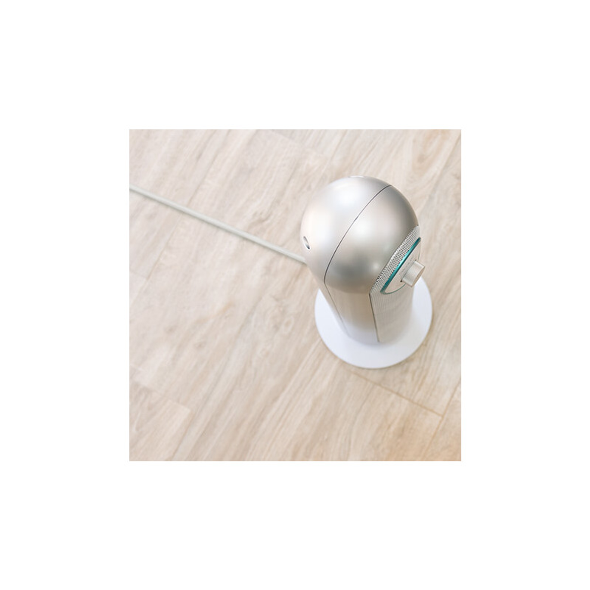 Srebrno-białe urządzenie z białą podstawą na drewnianej powierzchni. Kabel po lewej stronie.