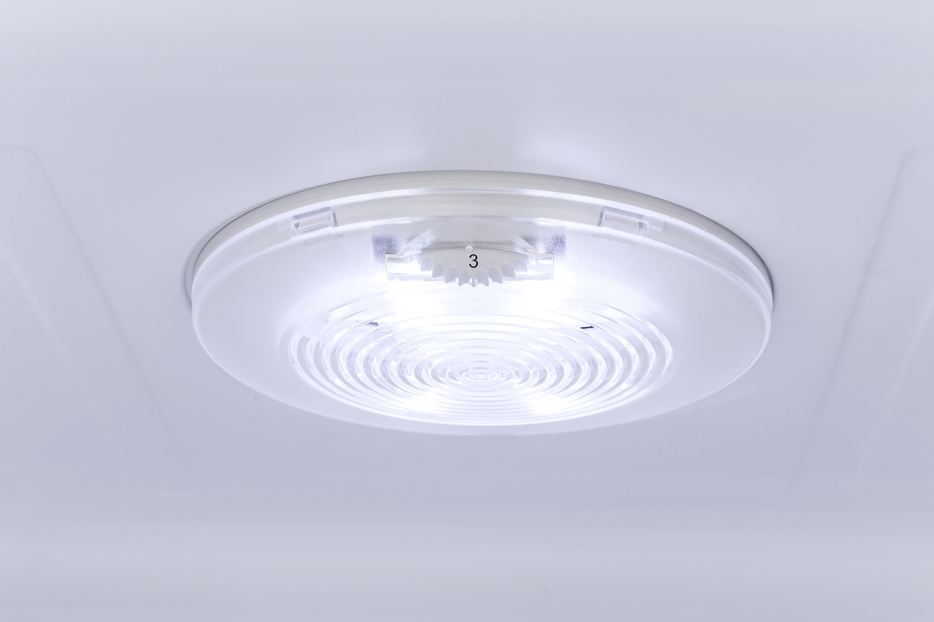 Nahaufnahme einer hellweißen Deckenleuchte. Das Licht ist kreisförmig und hat die Zahl 3 darauf.