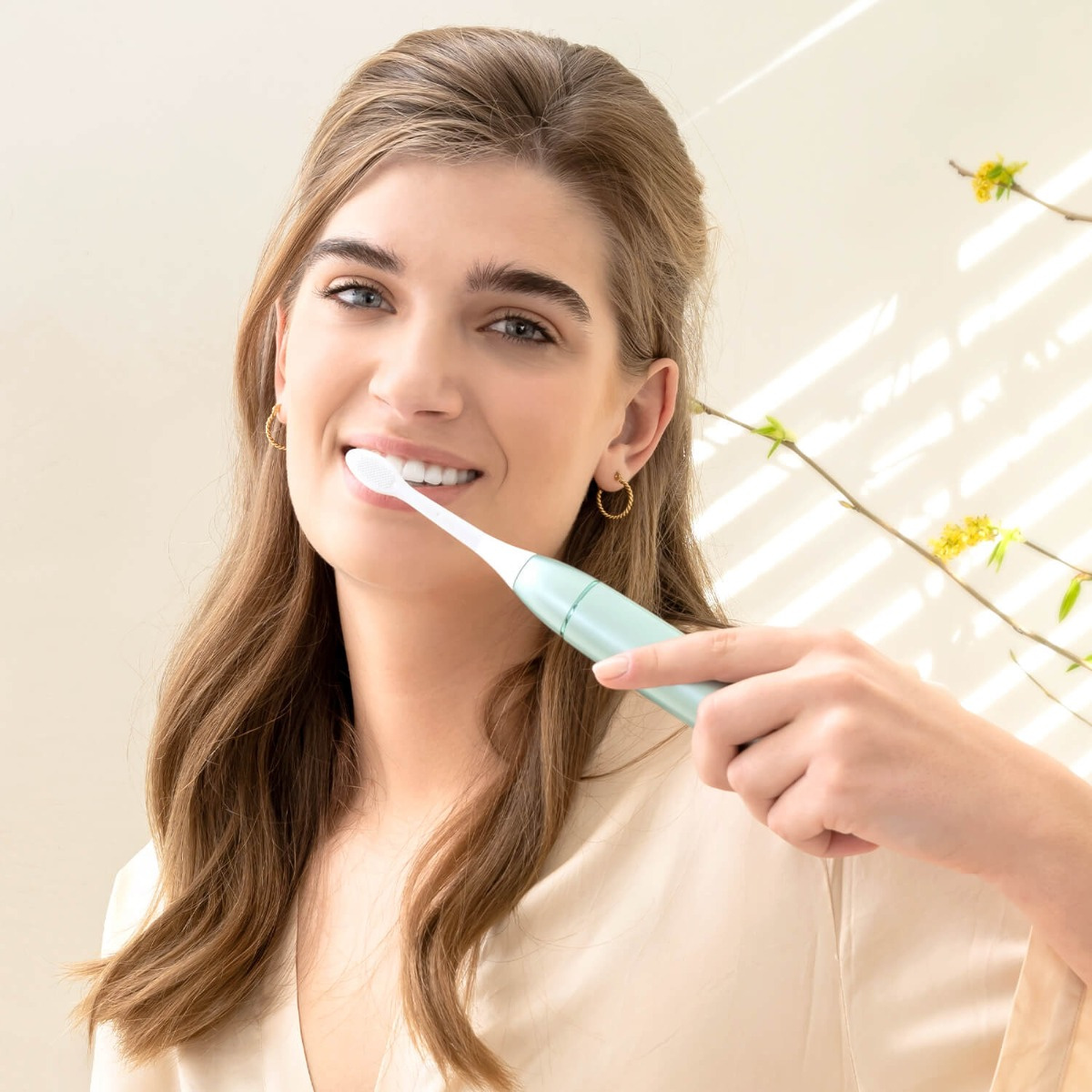 Kobieta myje zęby szczoteczką elektryczną, uśmiechając się i patrząc na widza.