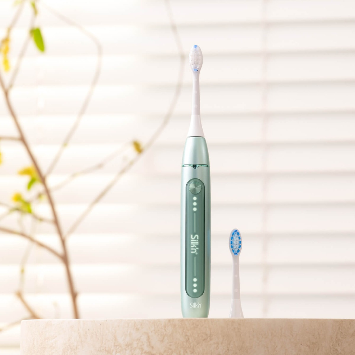 Zielona elektryczna szczoteczka do zębów i główka wymienna na marmurowej powierzchni.