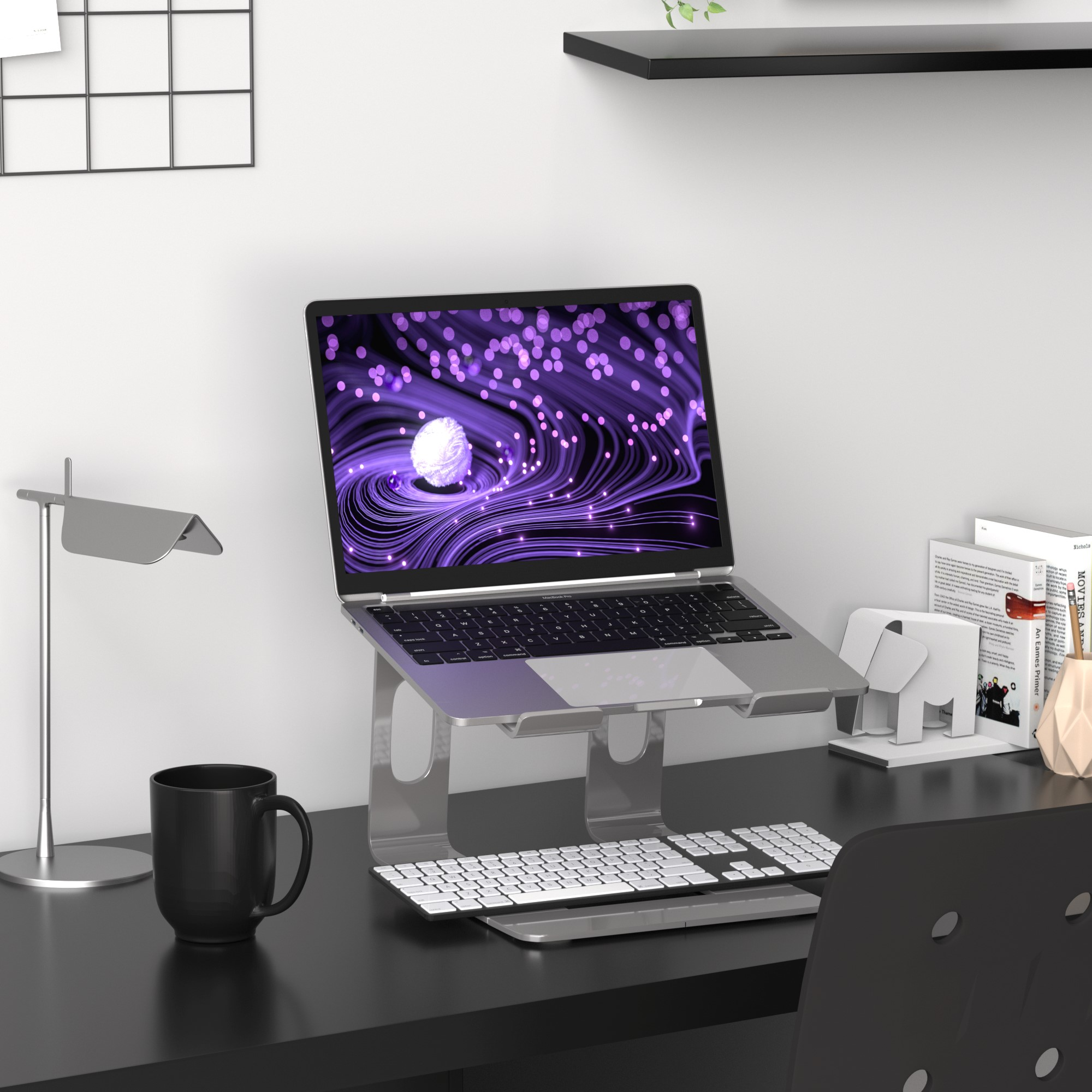 Laptop auf Ständer, Tastatur, Tasse und Dekoration auf schwarzem Schreibtisch, weiße Wand.