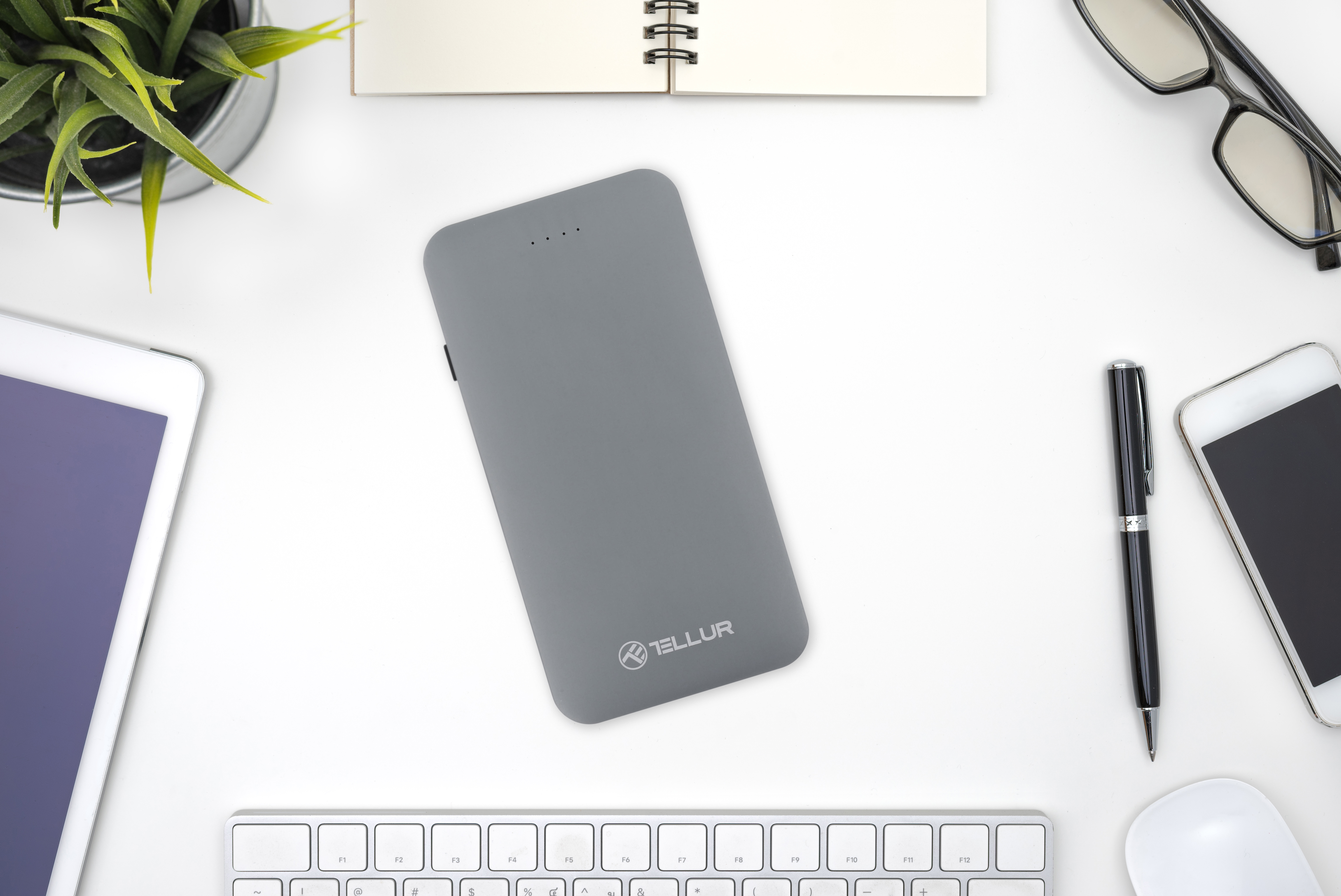 Szary power bank z białym tłem biurka. Inne przedmioty na biurku.