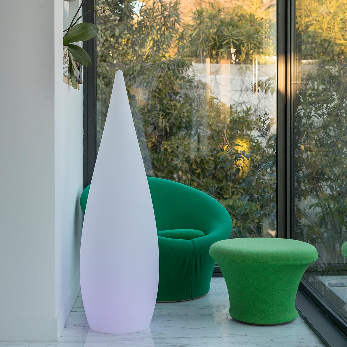 Eine weiße Stehlampe, grüner Stuhl und Hocker in einem modernen Raum mit großen Fenstern.