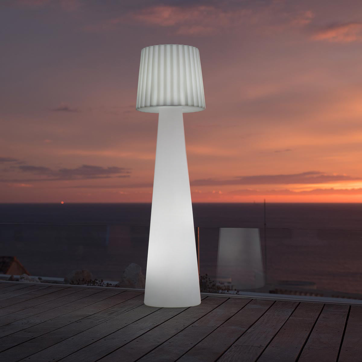 Eine weiße Außenlampe mit plissiertem Schirm. Der Hintergrund ist ein orange-blauer Sonnenuntergang.