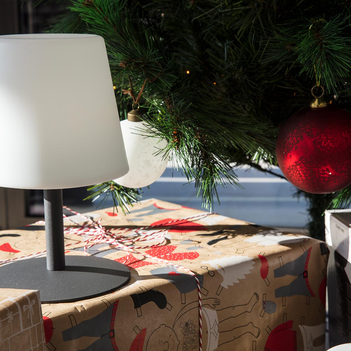 Weihnachtsbaum mit Ornamenten, einer weißen Lampe und darunter verpackten Geschenken.