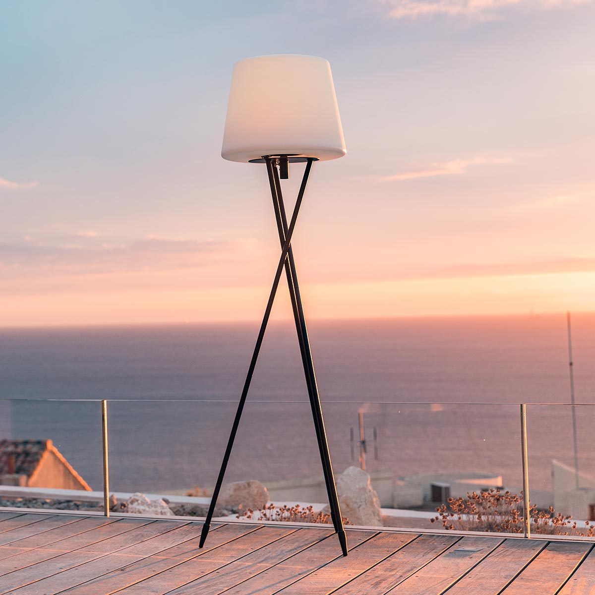 Stehlampe im Freien, weißer Schirm, schwarzer Rahmen, Holzdeck, Sonnenuntergang, Meer.