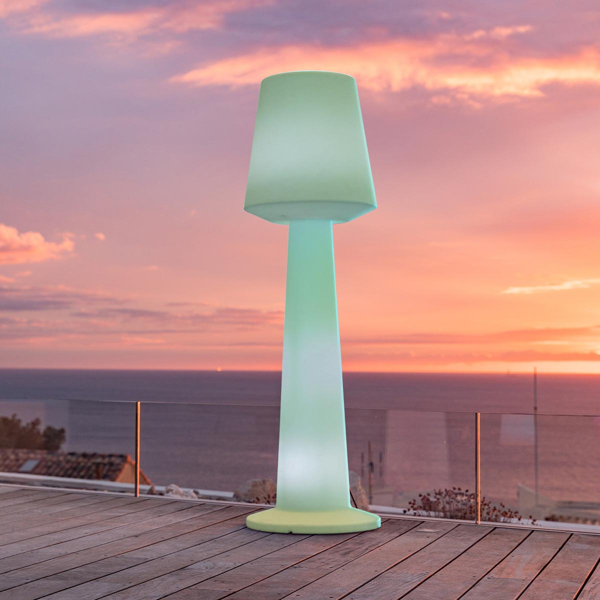 Hohe, beleuchtete Außenlampe auf einer Holzterrasse, mit Sonnenuntergang im Hintergrund.