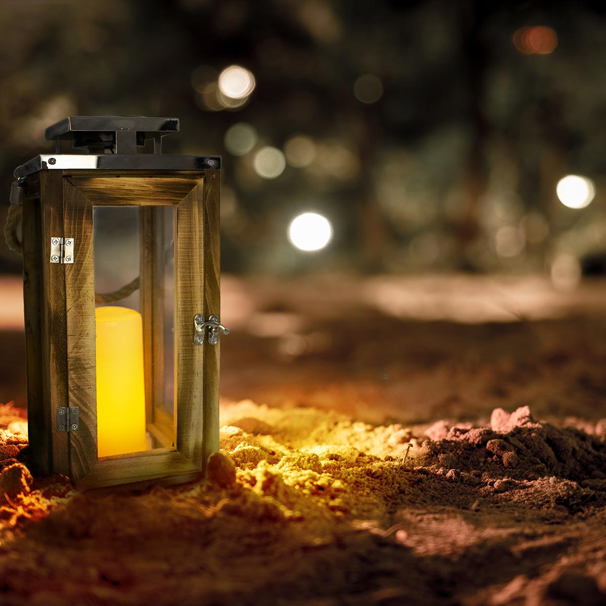 Holzlaterne mit brennender Kerze im Inneren, auf Sand. Verschwommener Hintergrund mit Bokeh-Lichtern.