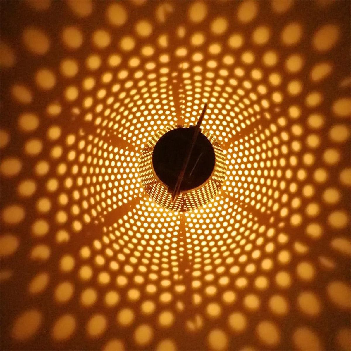 Nahaufnahme in einer Laterne mit einem gemusterten Design, das ein warmes, gepunktetes Lichtmuster wirft.