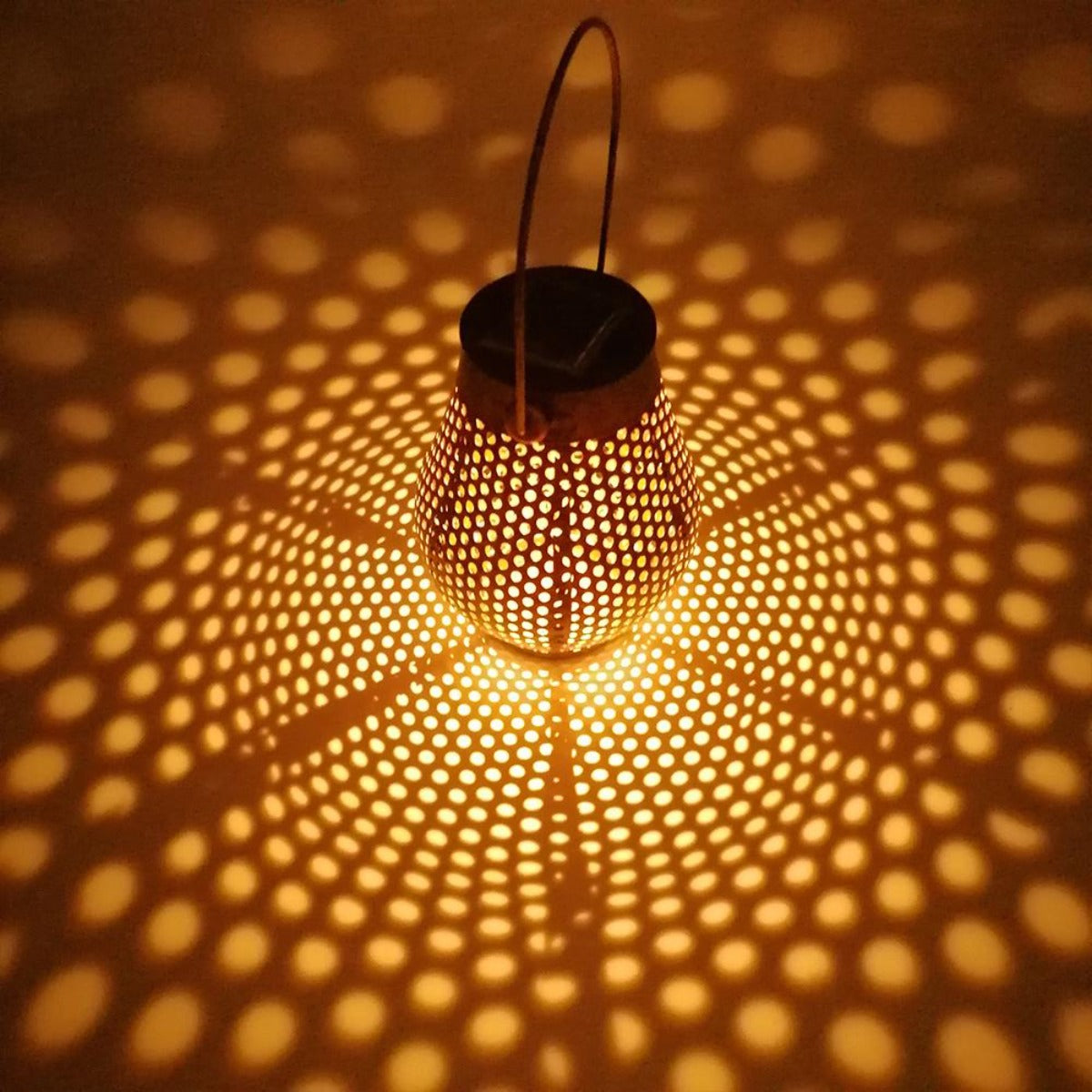 Solarbetriebene Laterne mit warmem Schein. Sie wirft einen gemusterten Schatten.