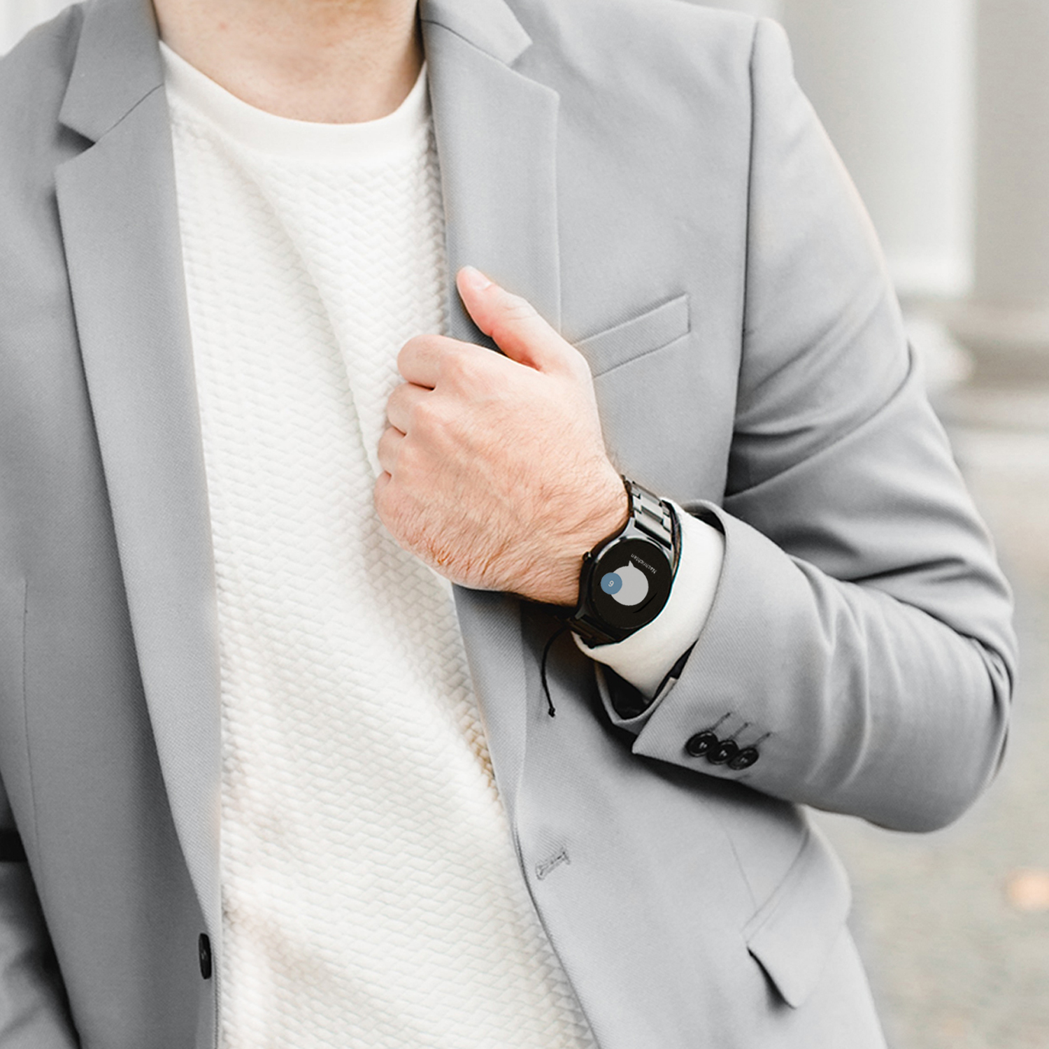 Ein Mann mit grauem Anzug und weißem Hemd. Er hat eine schwarze Uhr am Handgelenk.
