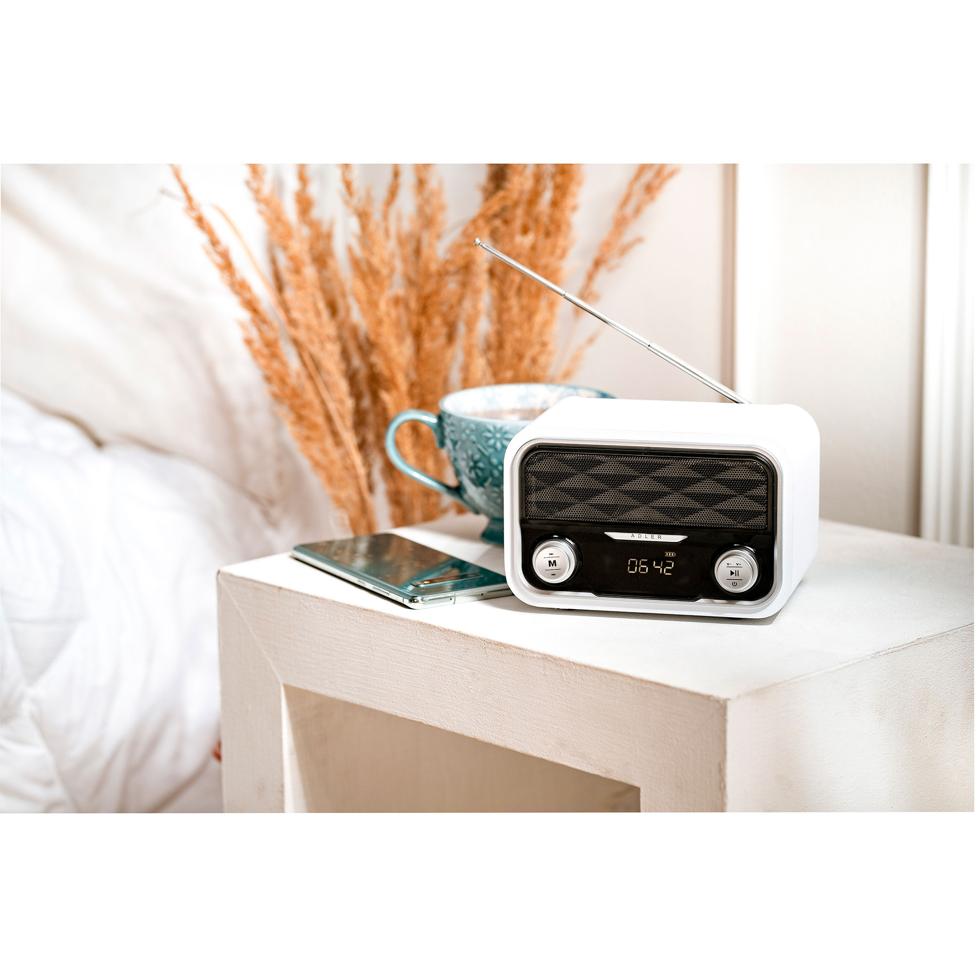 Radio bianca su un tavolo bianco con una tazza, un telefono e piante essiccate.