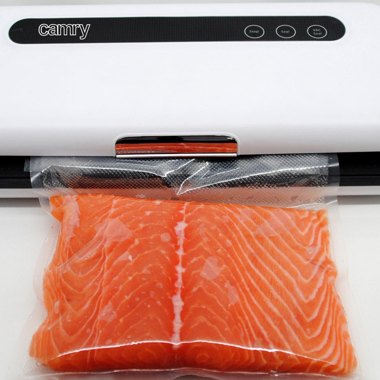 Zgrzewarka próżniowa z kawałkiem łososia w plastikowej torbie, na białej powierzchni.