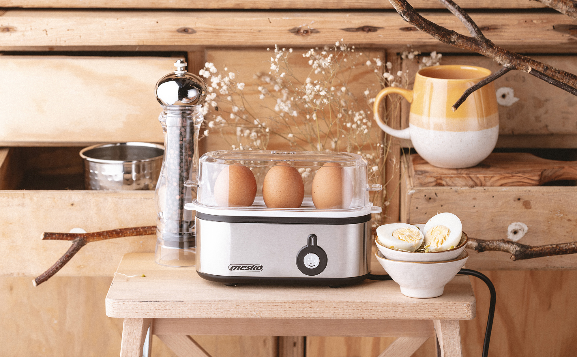 Jajka w parowarze do jajek, kubek, młynek do pieprzu i miska z pokrojonymi jajkami.