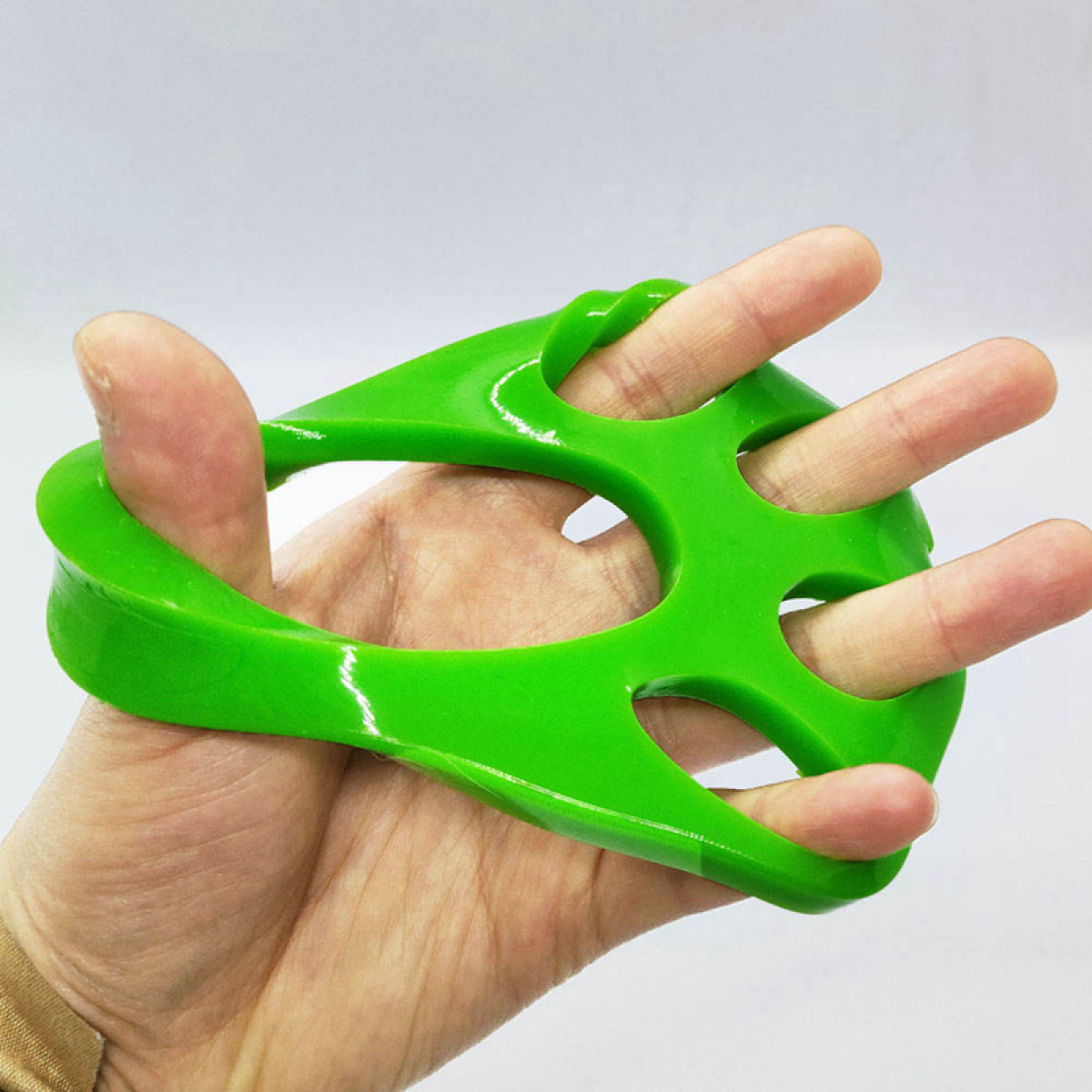 Eine Hand hält einen grünen Finger-Trainer. Finger werden durch Löcher gesteckt. Weißer Hintergrund.