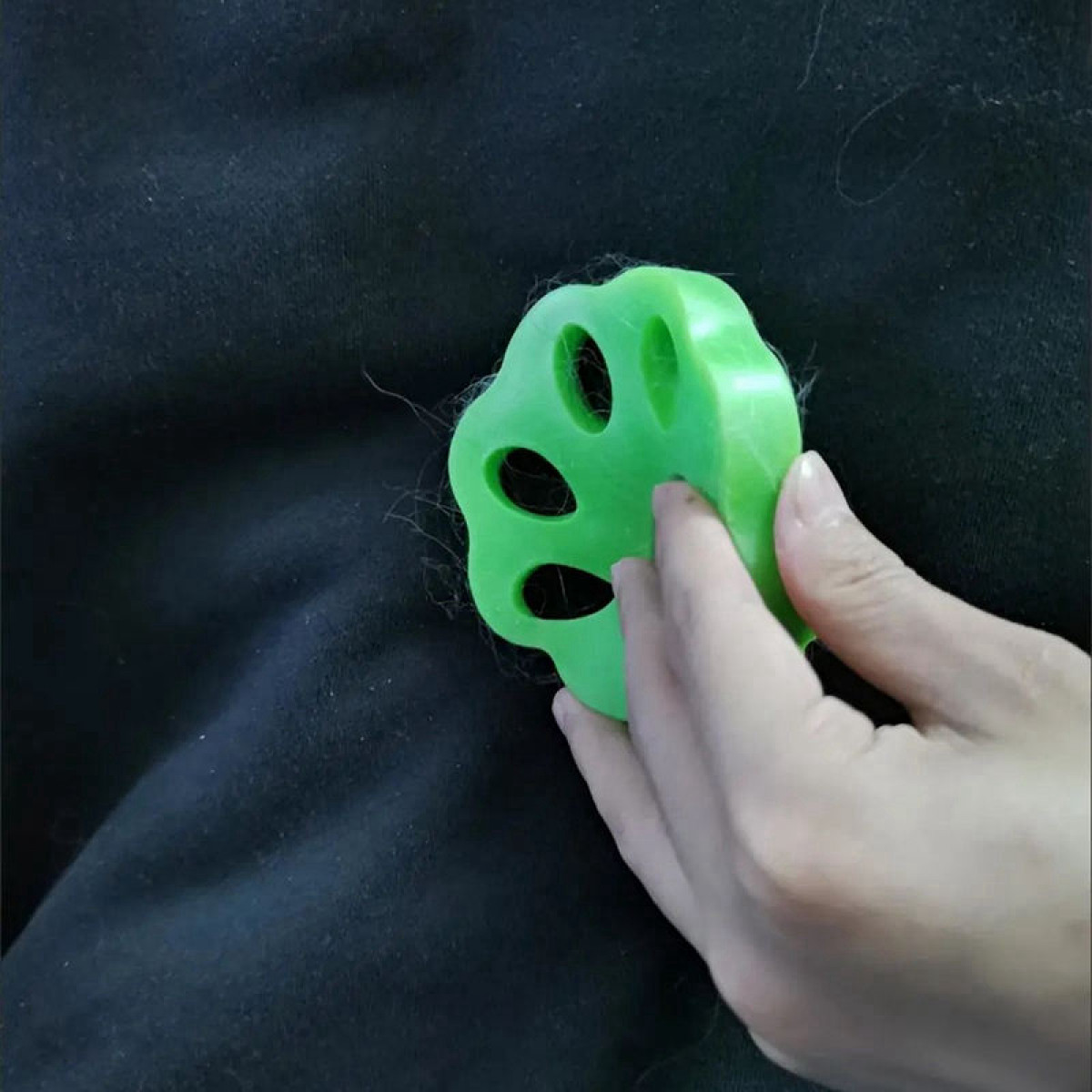 Ein grüner Tierhaarentferner, mit einer Hand, die ihn über einer schwarzen Oberfläche hält.