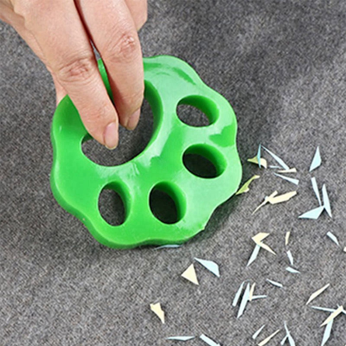 Eine Hand hält einen grünen, pfotenförmigen Fusselentferner über Grauem mit Schmutz.
