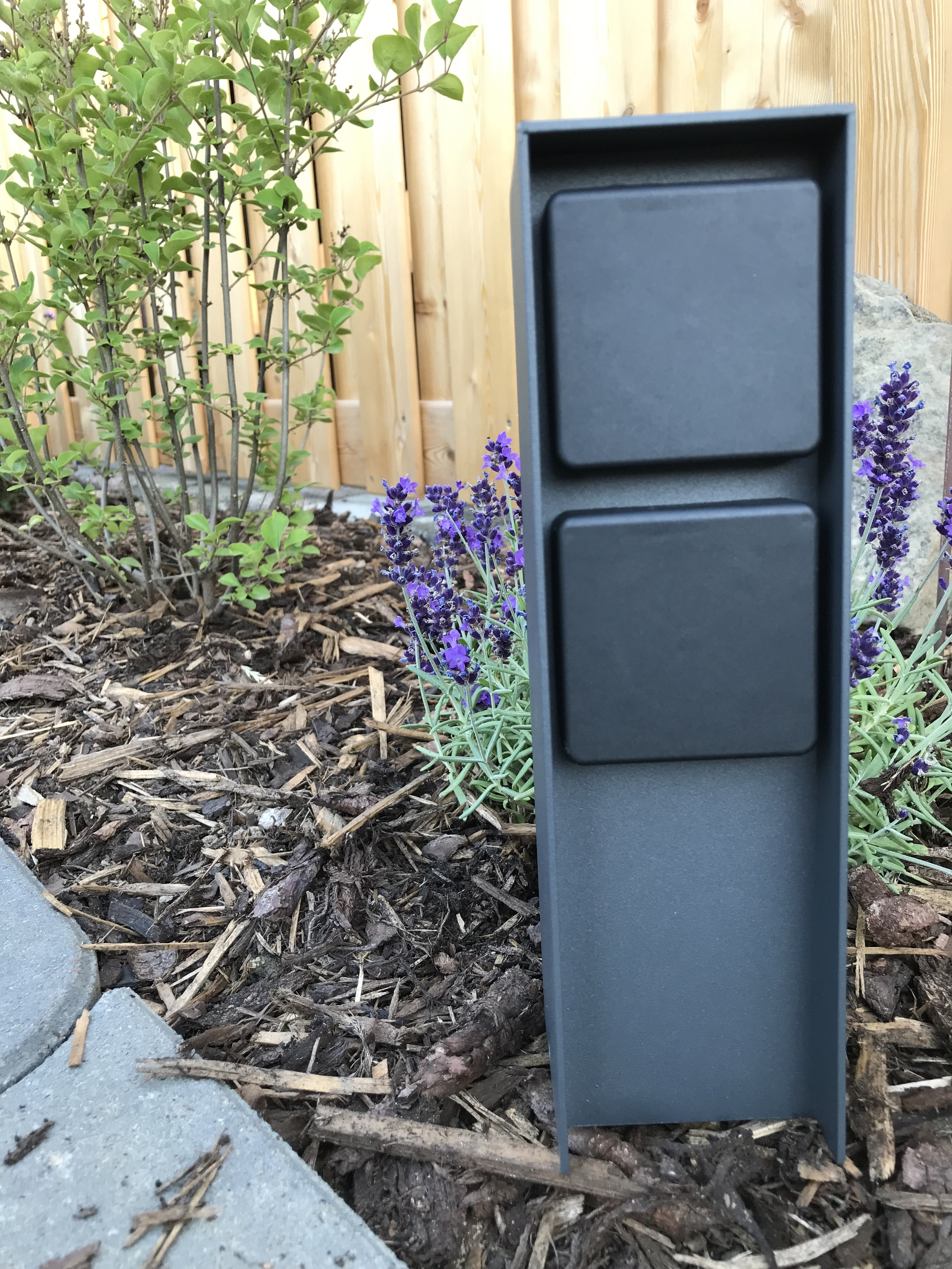 Schwarzer Metallpfosten mit zwei quadratischen Paneelen. Lavendel und Mulch im Hintergrund.