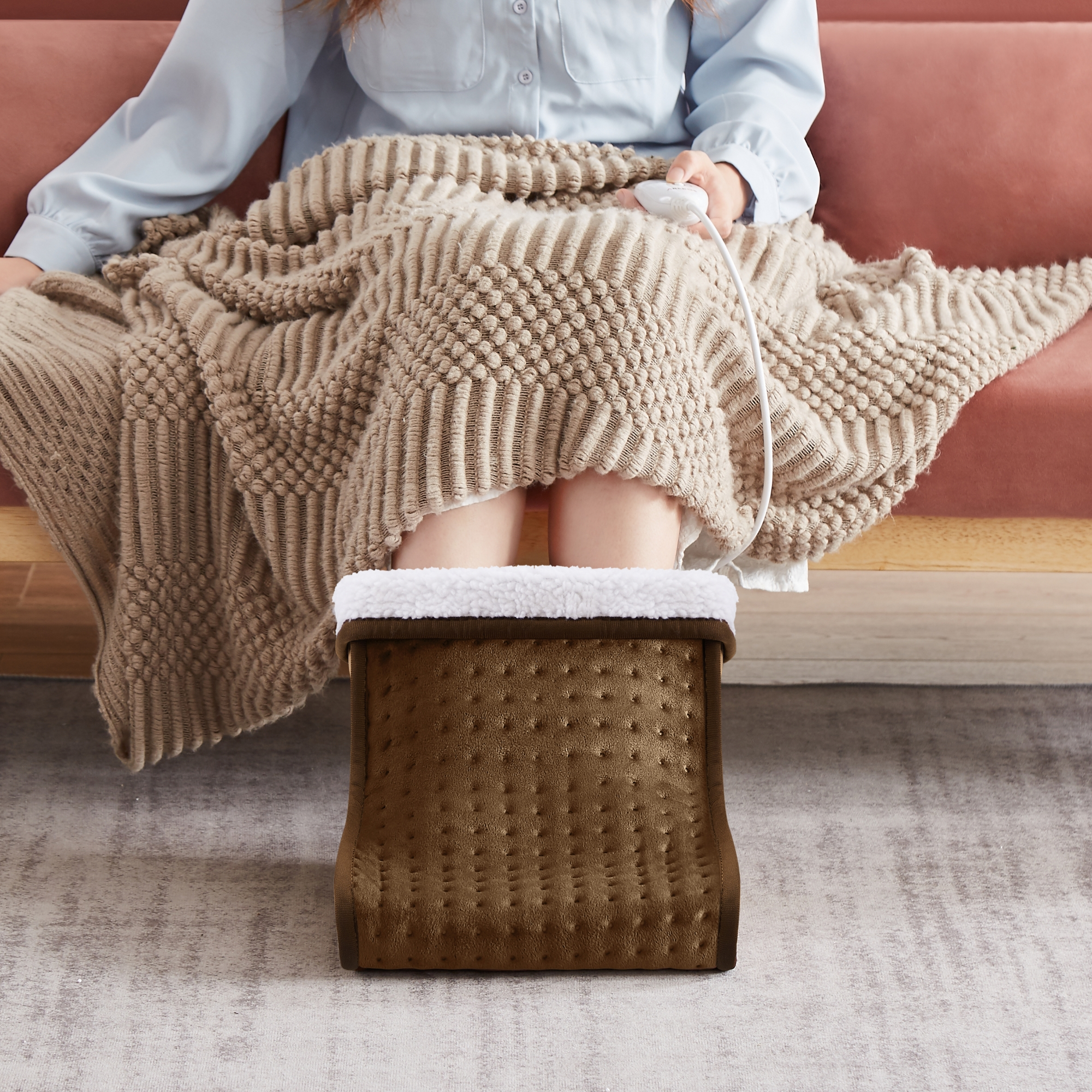 Frau auf einem Sofa mit einem Fußwärmer. Sie hält die Fernbedienung.