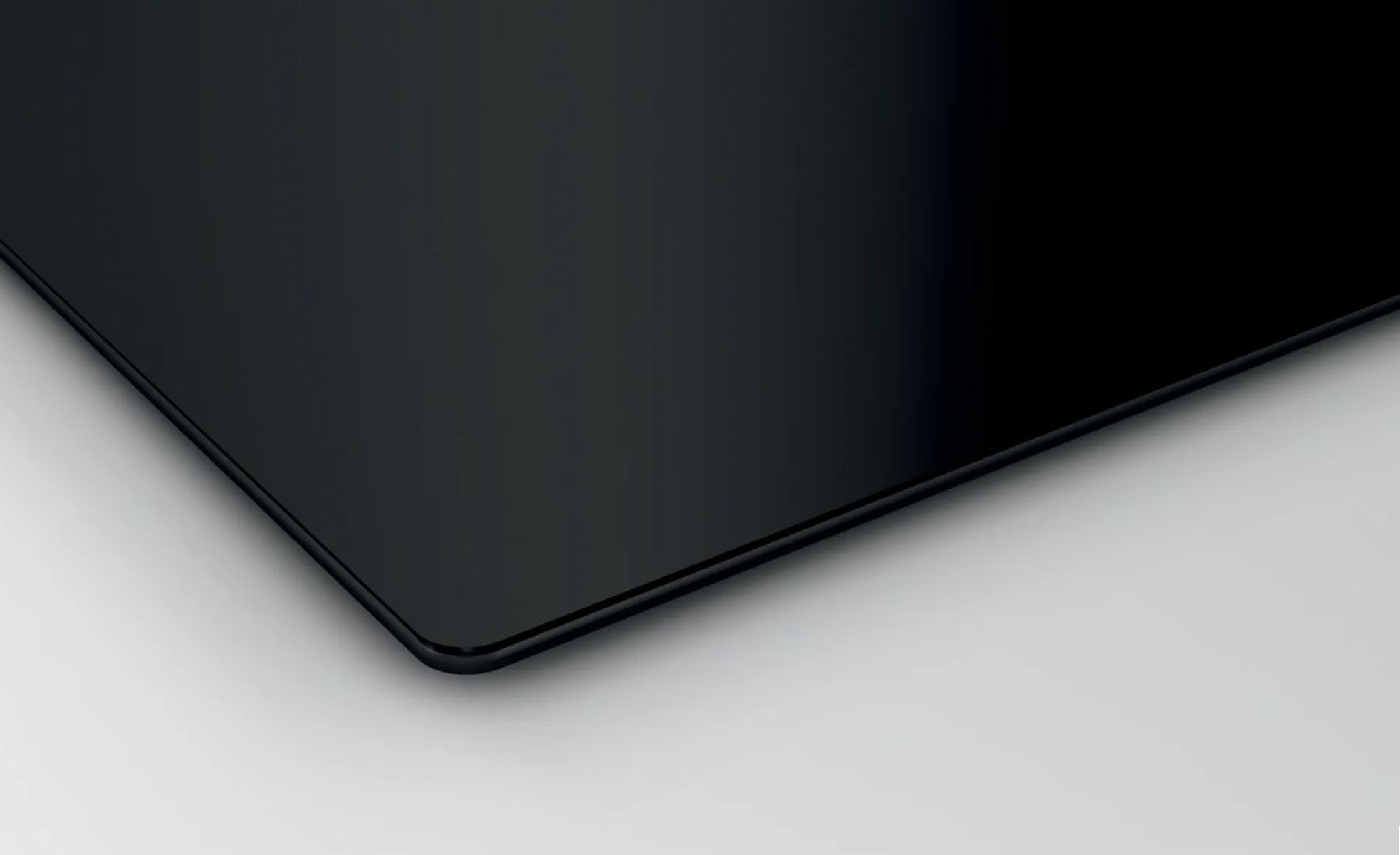 Czarna szklana płyta grzewcza z błyszczącą powierzchnią. Powierzchnia odbija białe tło.