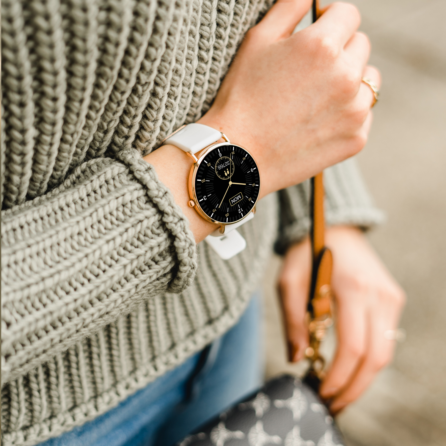 Das Handgelenk einer Frau mit einer weißen Uhr, goldfarbener Einfassung. Das Zifferblatt ist schwarz. Der Hintergrund ist unscharf.