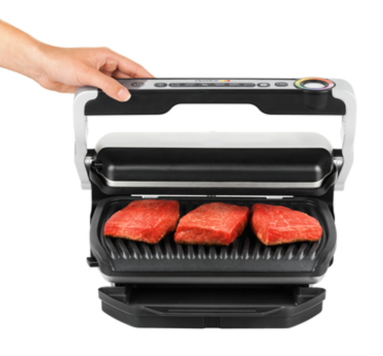 Parrilla eléctrica con tres trozos de carne cruda. Mano sosteniendo el asa.