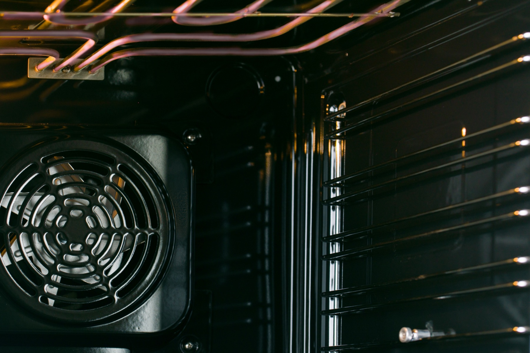 Interior de un horno negro. Ventilador a la izquierda, elementos calefactores arriba. Rejillas metálicas dentro.