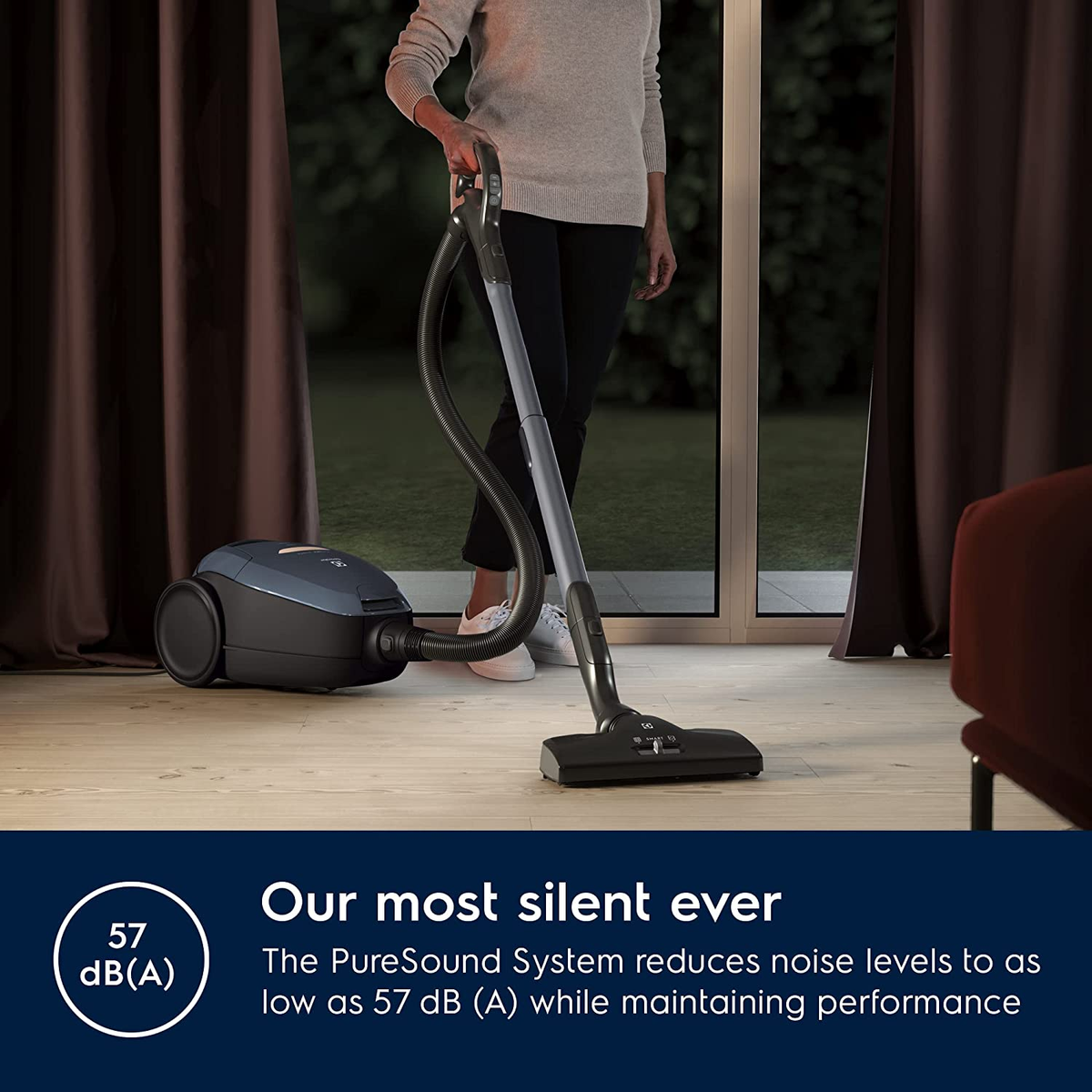 Osoba odkurza czarno-niebieskim odkurzaczem. Tekst: Nasz najcichszy w historii.