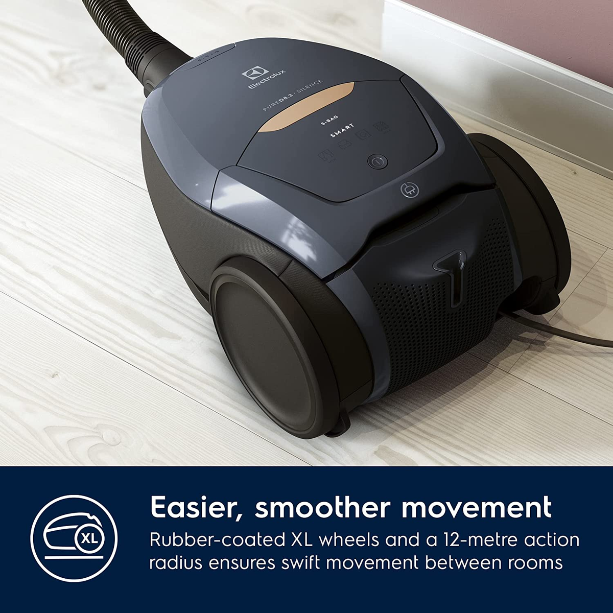 Ciemnoszary odkurzacz z wężem i kołami XL, na drewnianej podłodze, z tekstem o ruchu.