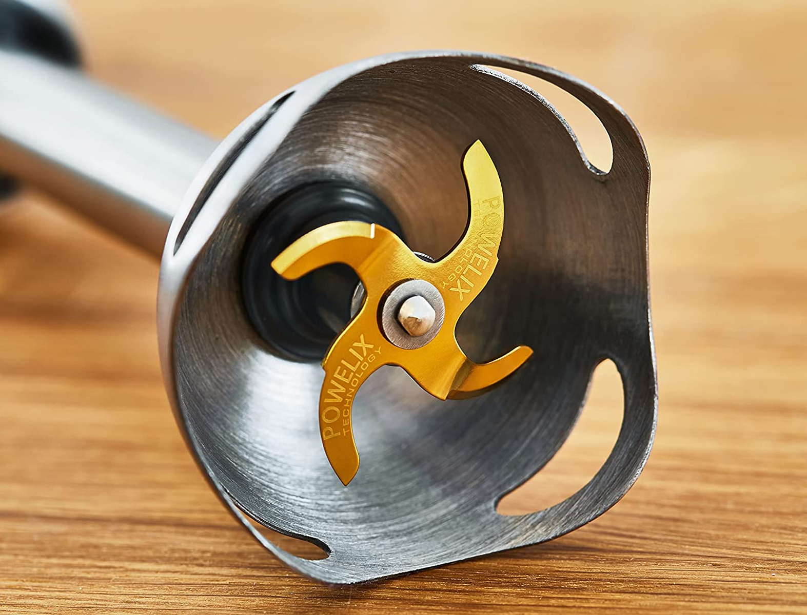 Zbliżenie na srebrną i złotą głowicę blendera ręcznego. Ostrza są złote.