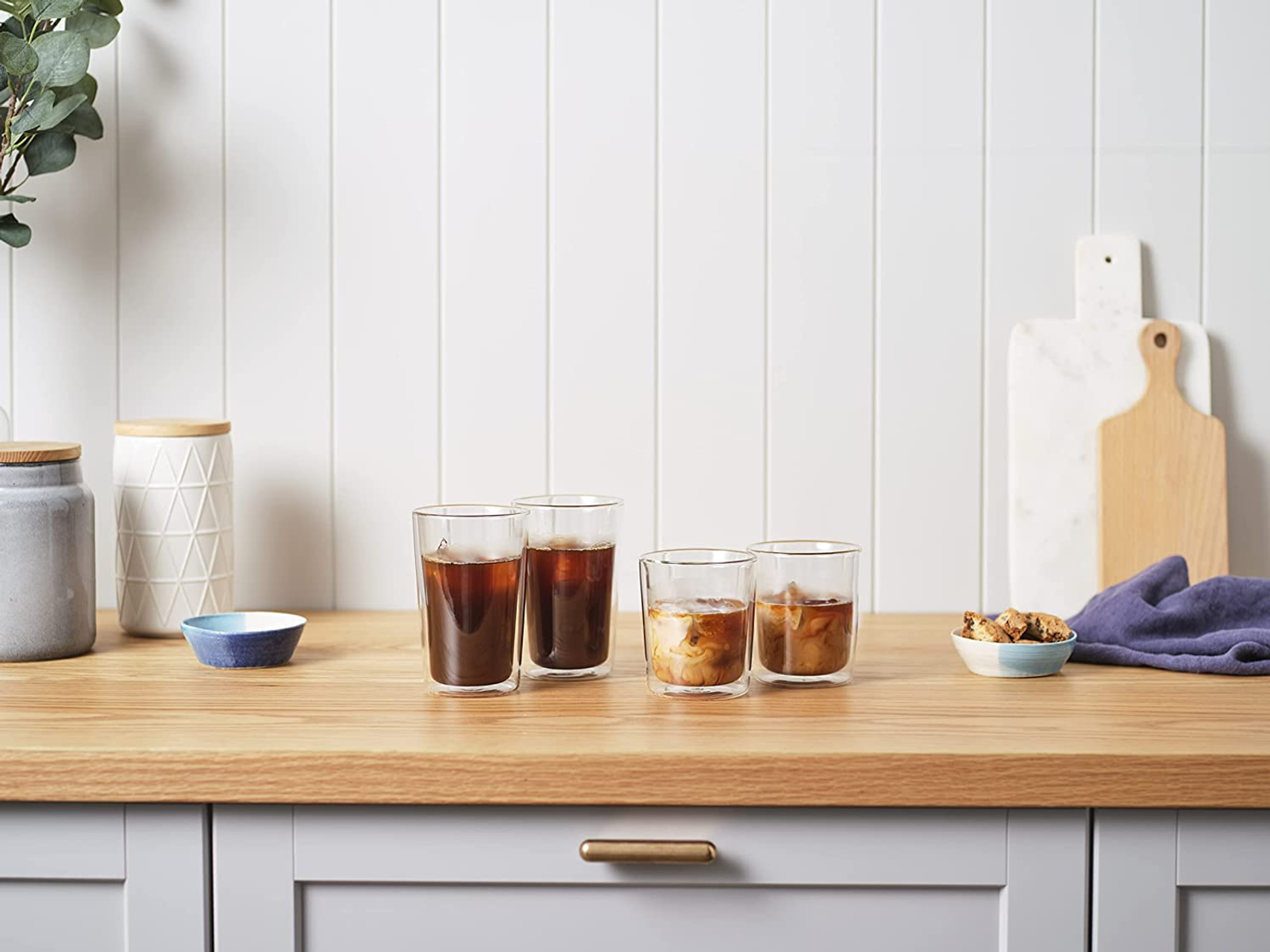 Vier Gläser Eiskaffee auf einer Holzoberfläche. Weißer Hintergrund mit weißer Wand und einigen Requisiten.