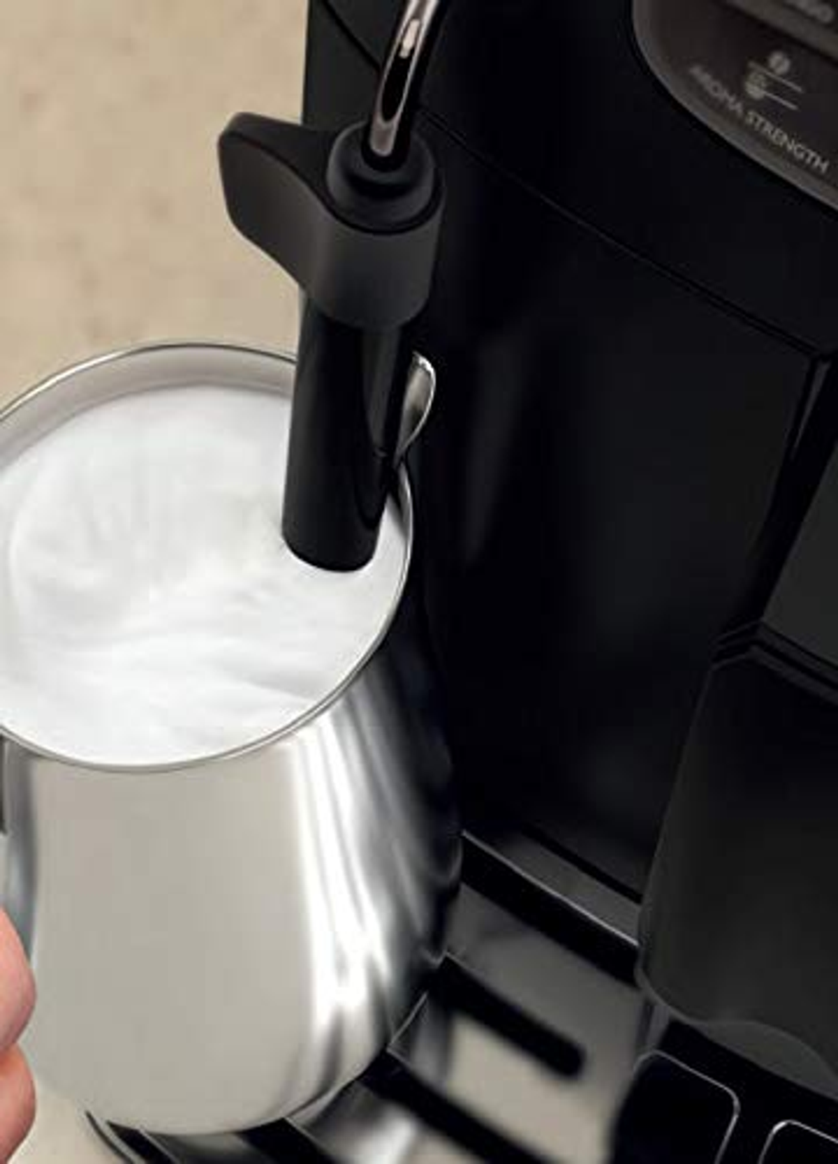 Melk opschuimen in zilveren kan, zwarte koffiemachine op de achtergrond.