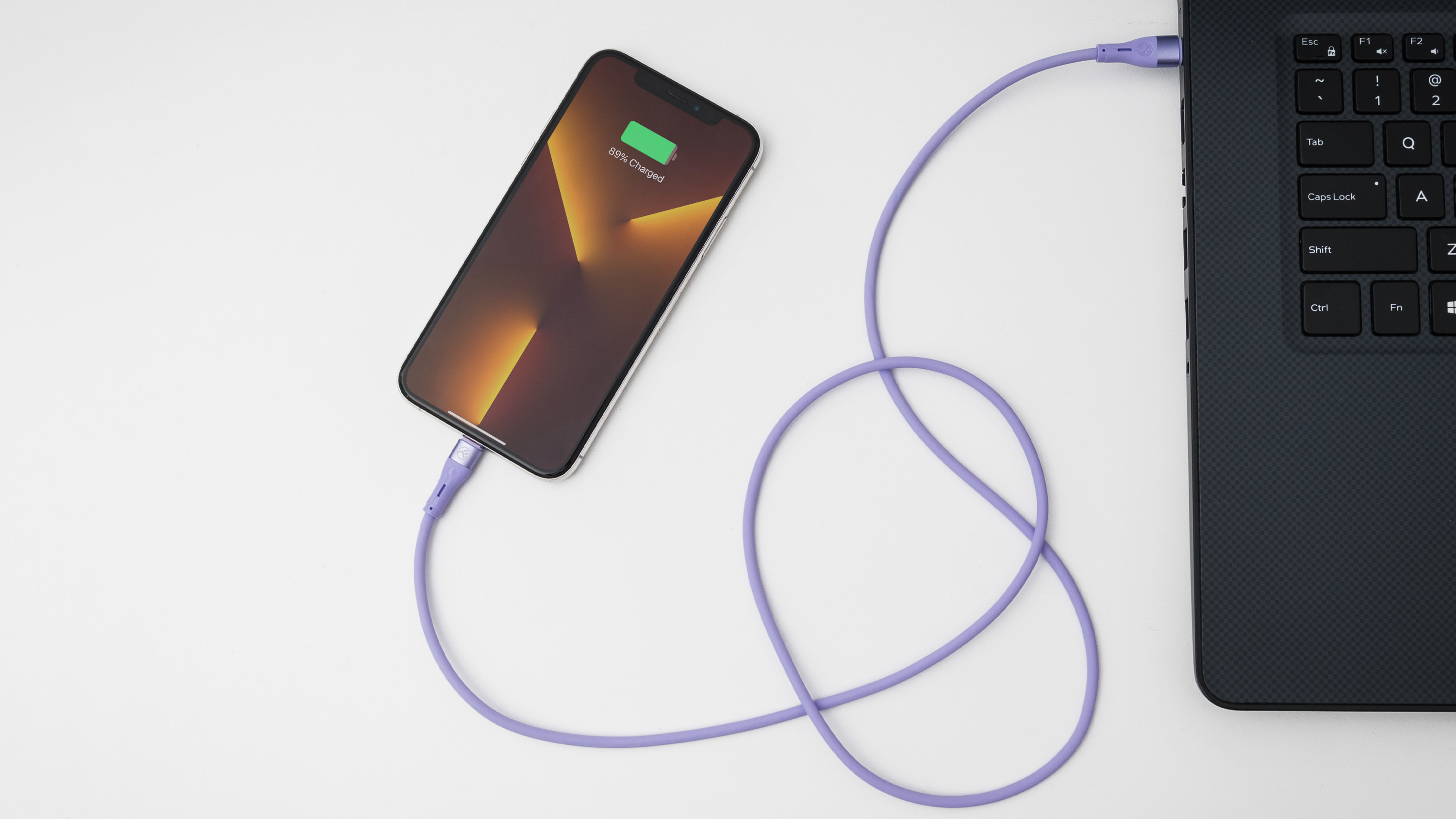 Telefon ładujący się na laptopie za pomocą fioletowego kabla ładującego.