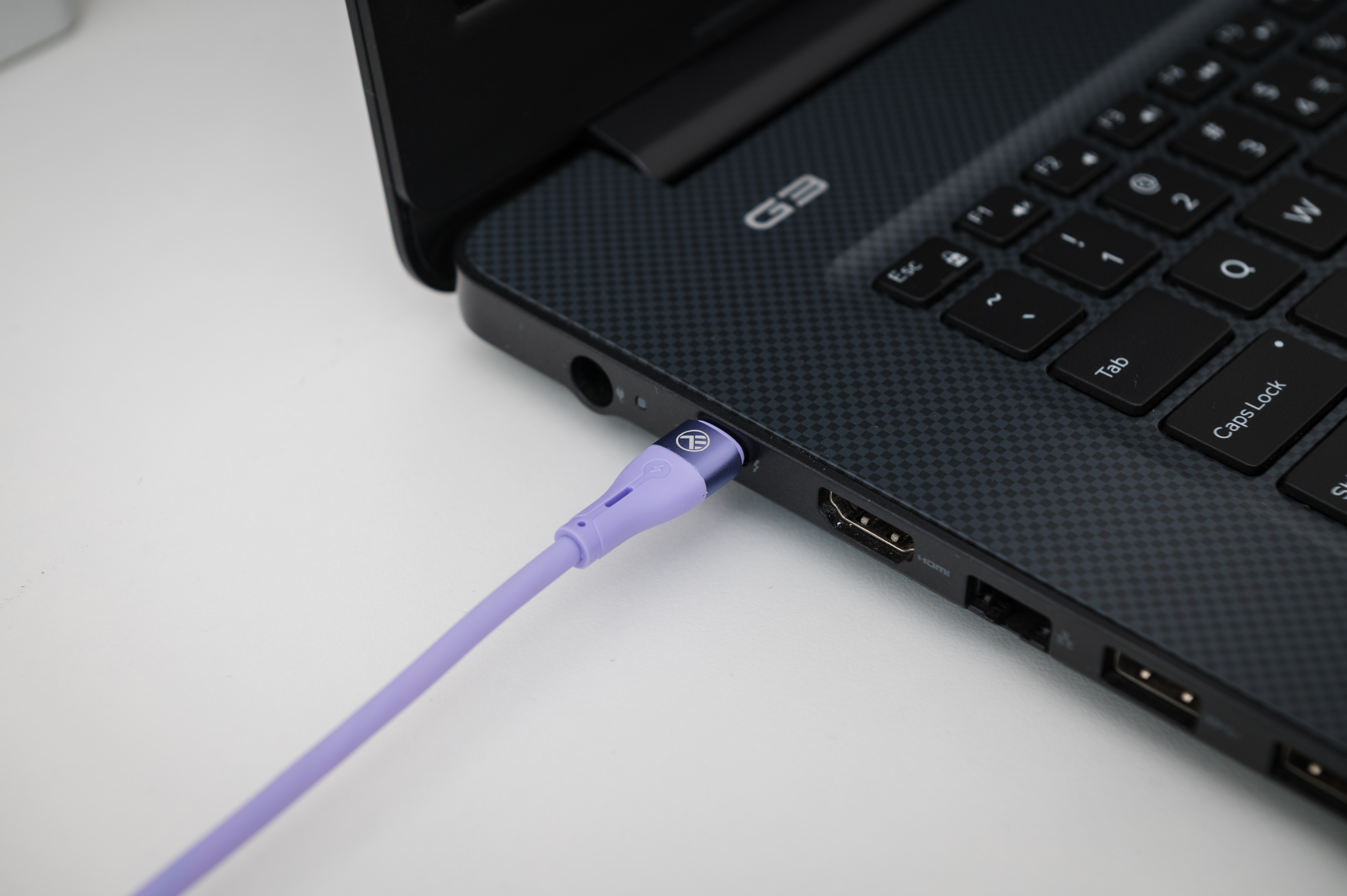 Jasnofioletowy kabel ładujący USB-C jest podłączony do laptopa.