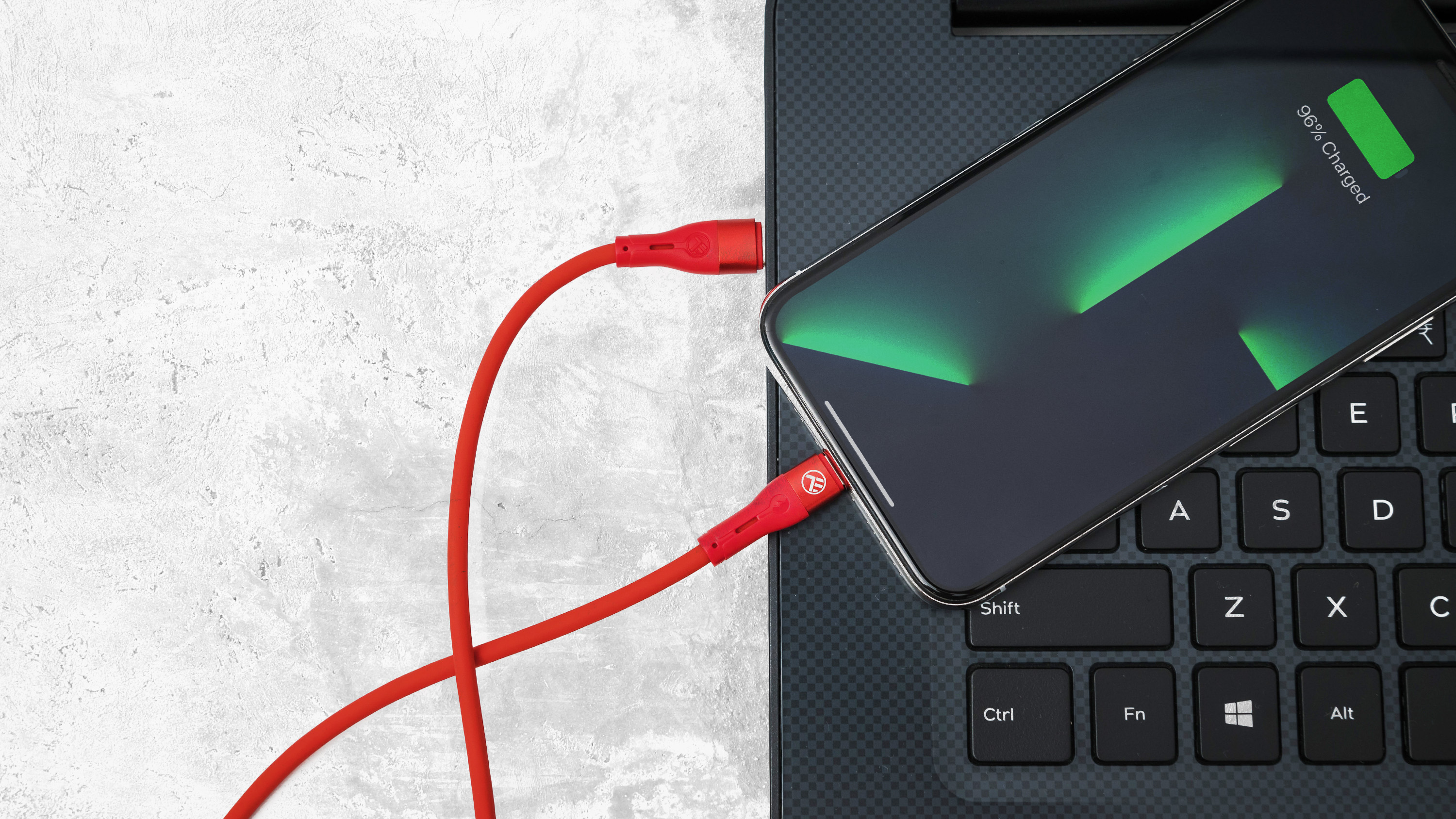 Telefon ładujący się na laptopie z czerwonym kablem ładującym.