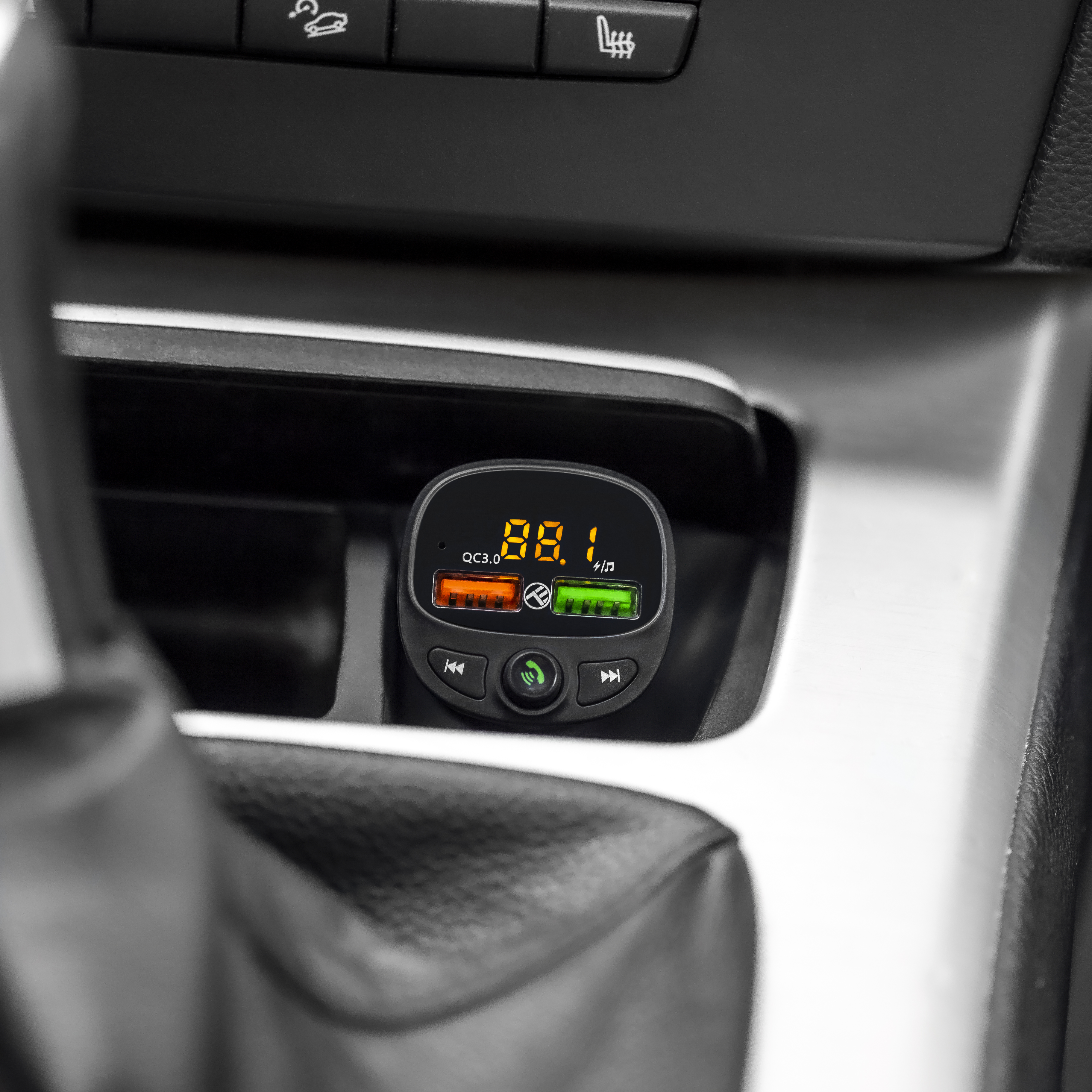 Cargador de coche con pantalla, mostrando frecuencia FM y otra información.