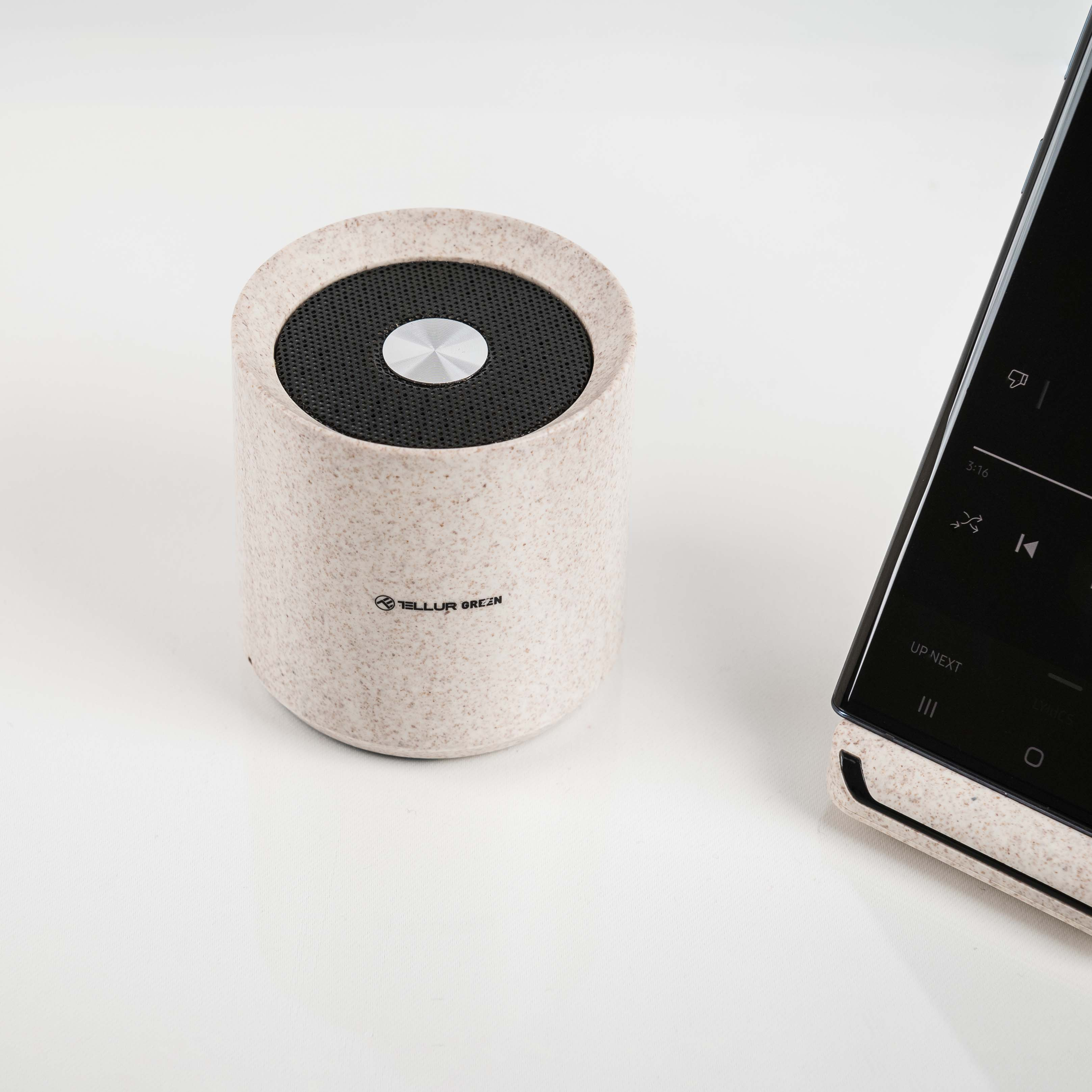 Beżowy głośnik i smartfon znajdują się na białym tle. Głośnik ma czarną siatkę, a telefon jest czarny.