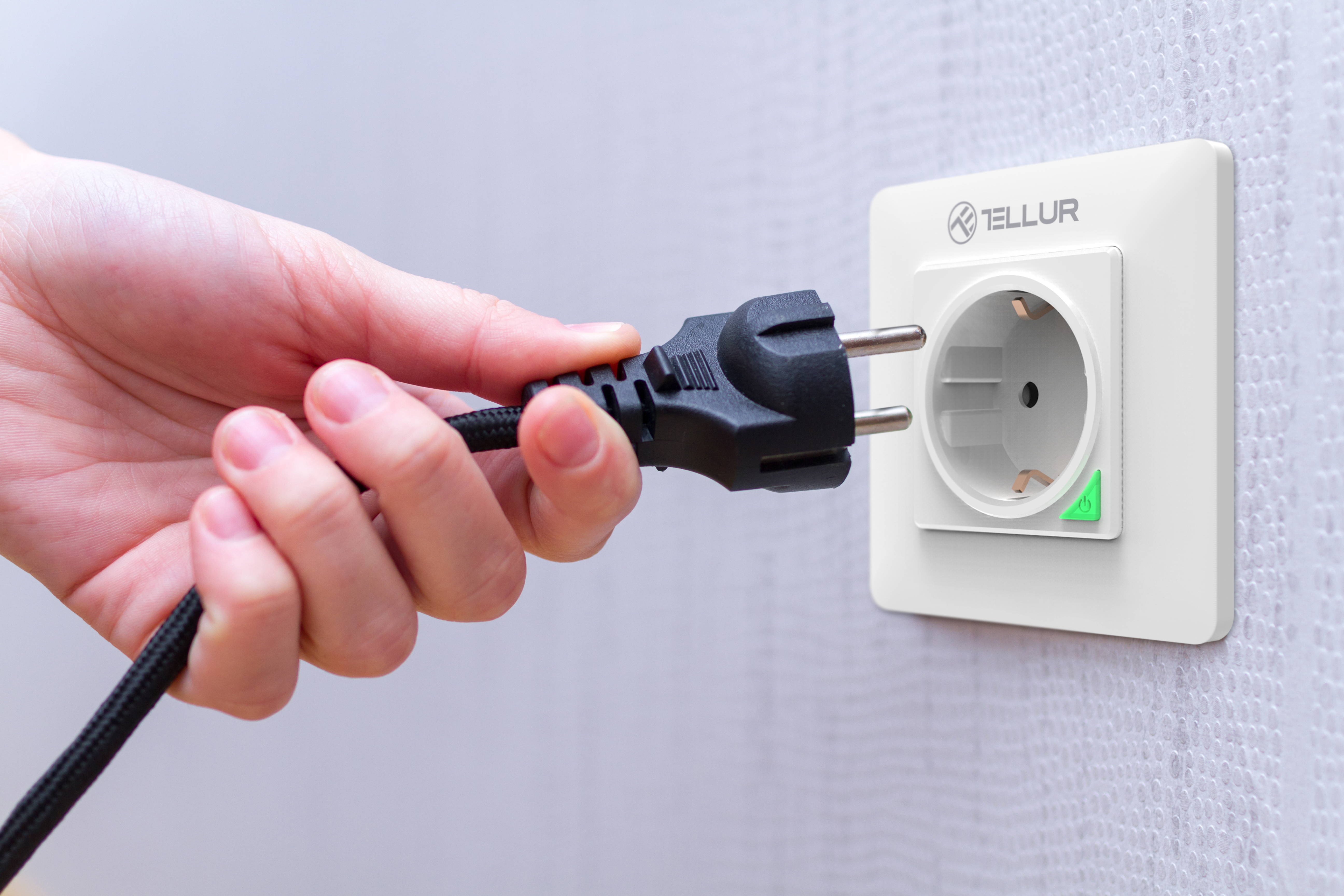 Hand steckt schwarzen Stecker in weiße Steckdose, die Steckdose ist von der Marke Tellur.
