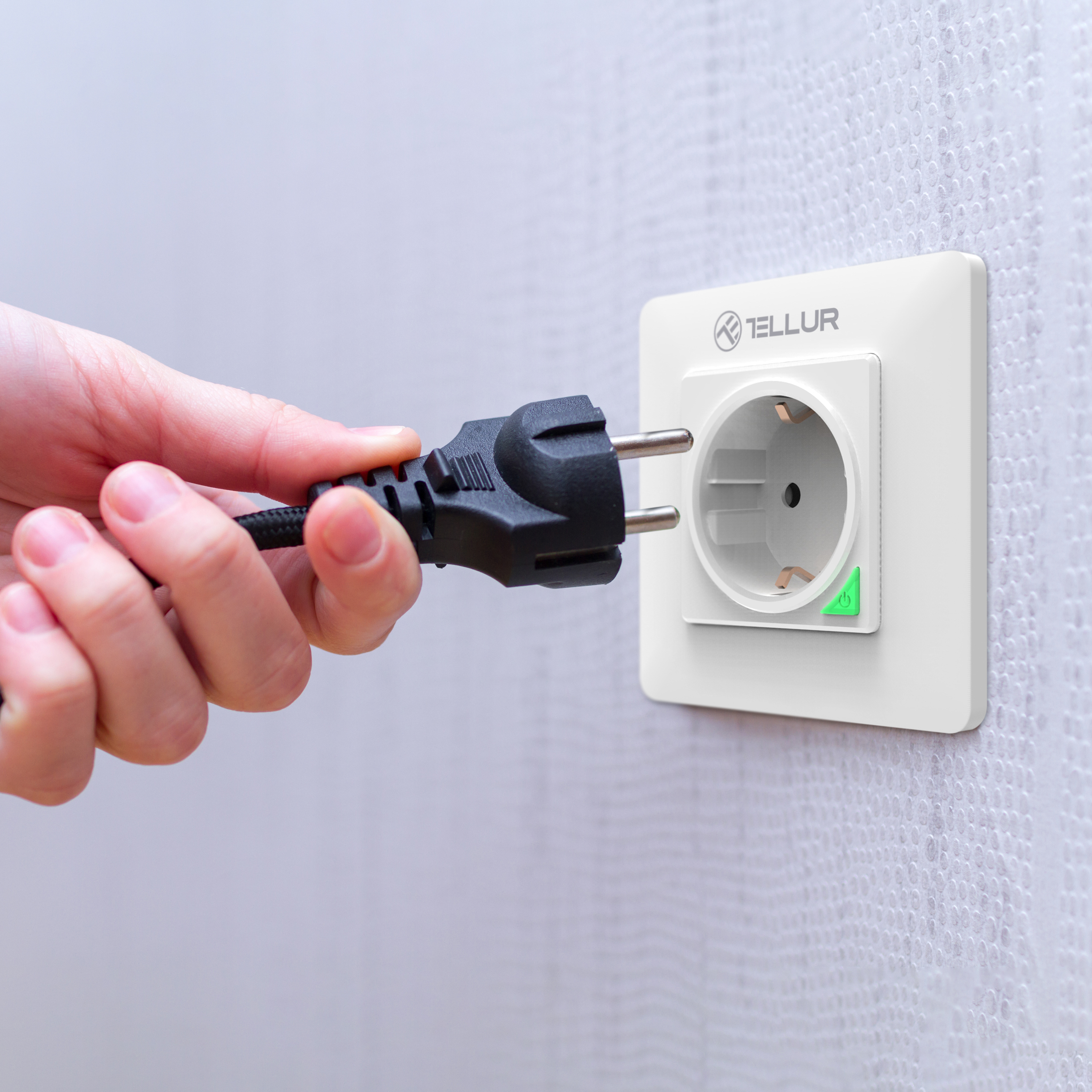 Hand steckt schwarzen Stecker in weiße Steckdose. Tellur-Logo auf der Steckdose.
