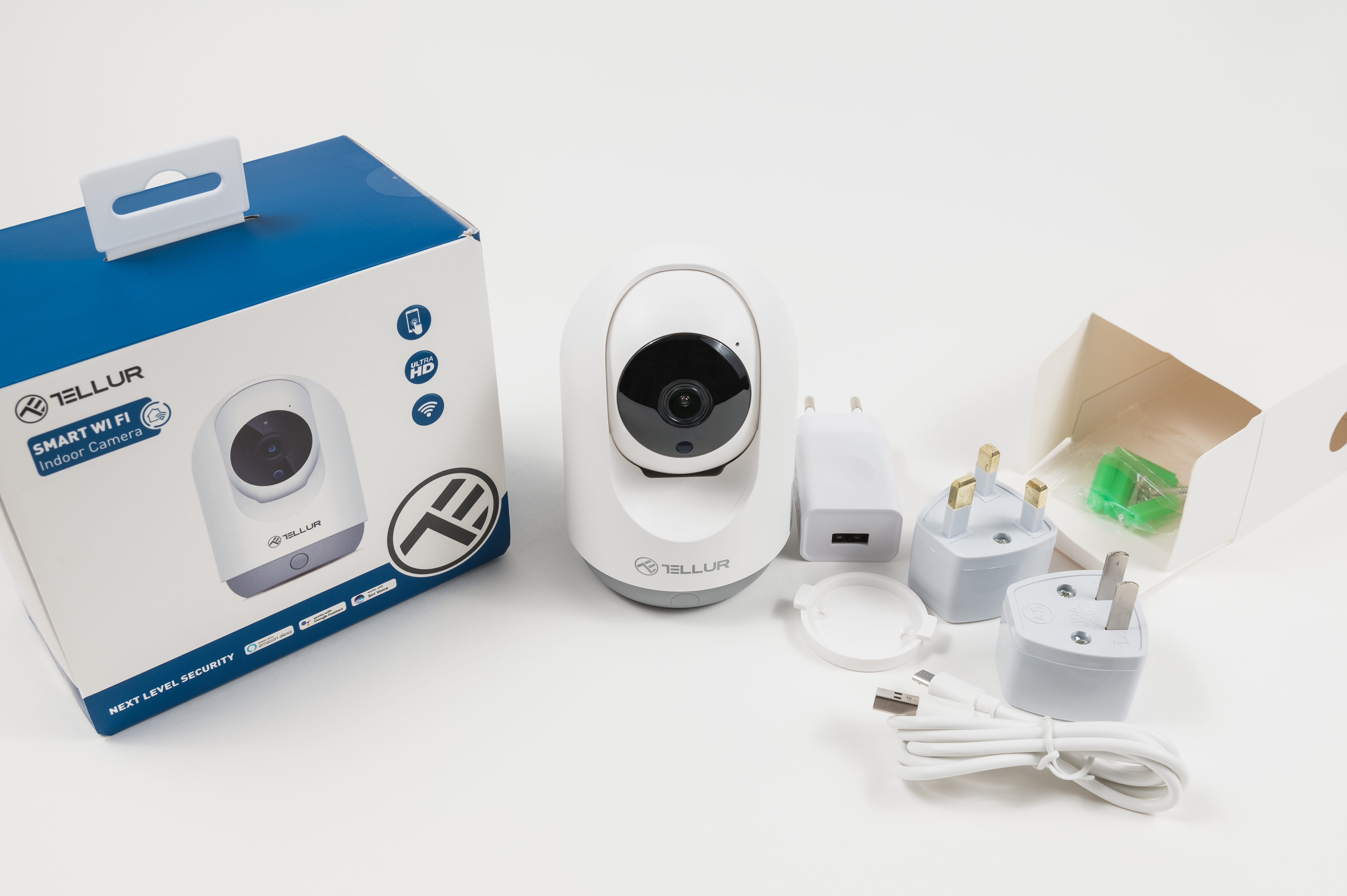 Biały zestaw kamery wewnętrznej Wi-Fi Tellur Smart z pudełkiem, wtyczkami i akcesoriami na białej powierzchni.