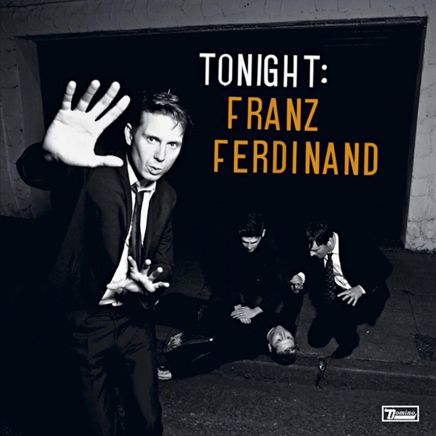 Bild von Franz Ferdinand. Ein Mann im Anzug mit erhobener Hand und eine Gruppe Männer im Hintergrund.
