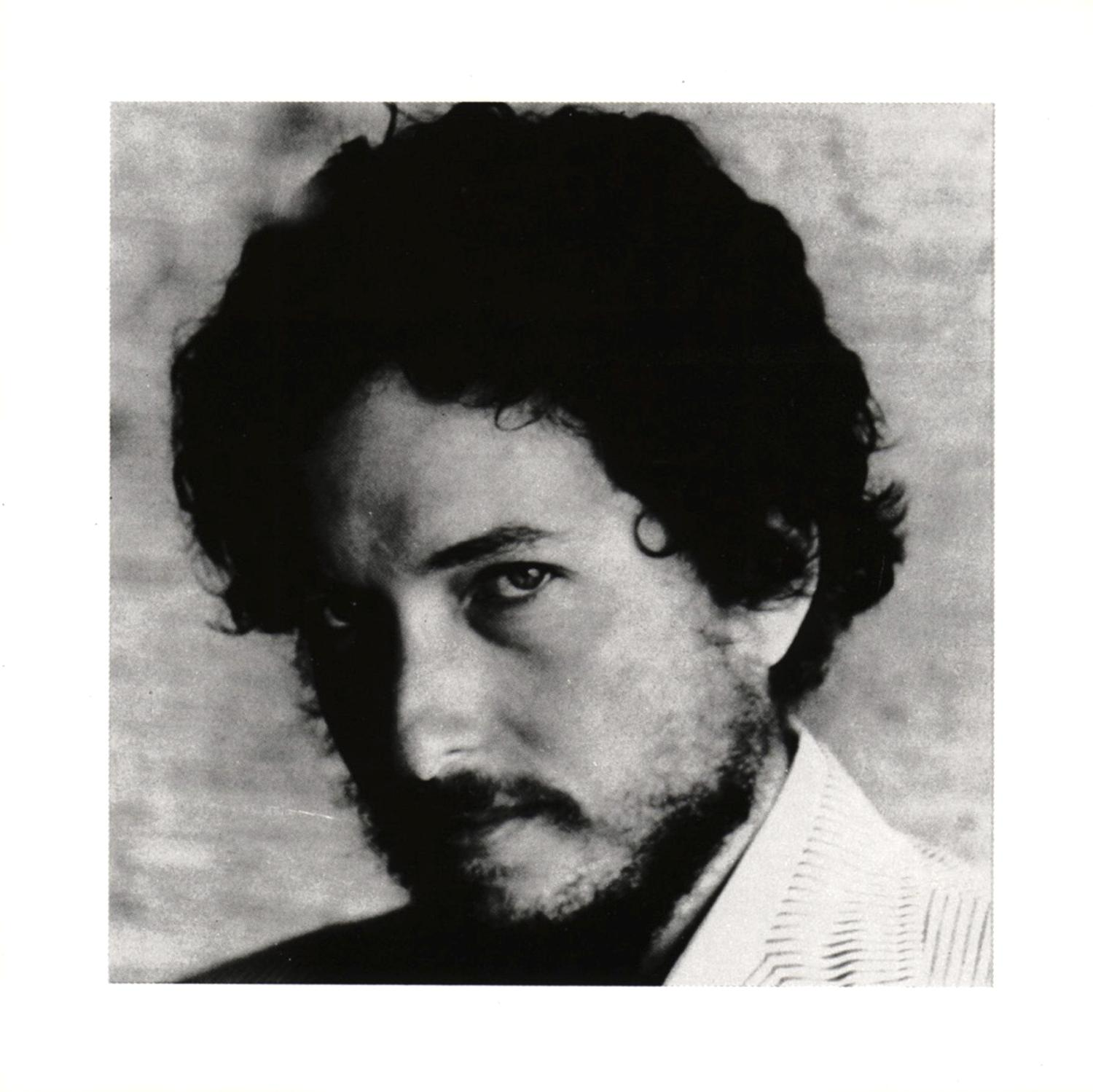 Schwarz-Weiß-Porträt von Bob Dylan, der den Betrachter mit Bart und lockigem Haar ansieht.