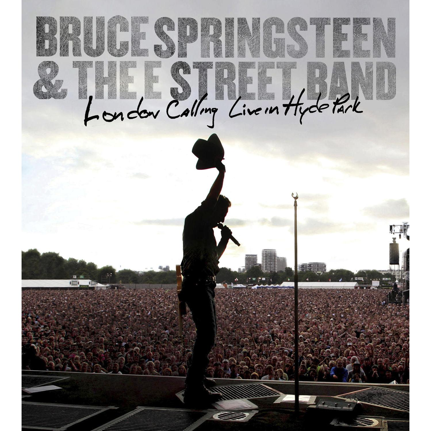 Bruce Springsteen auf der Bühne, hebt einen Hut. Menge im Hintergrund.