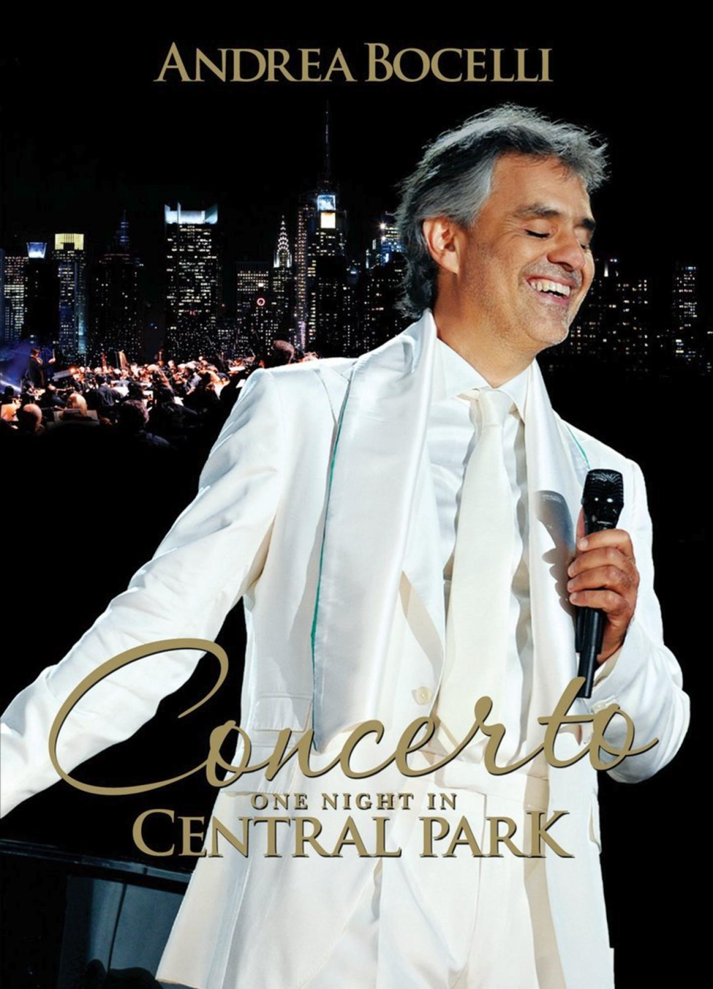 Andrea Bocelli im weißen Anzug singt nachts auf der Bühne, mit Skyline im Hintergrund.