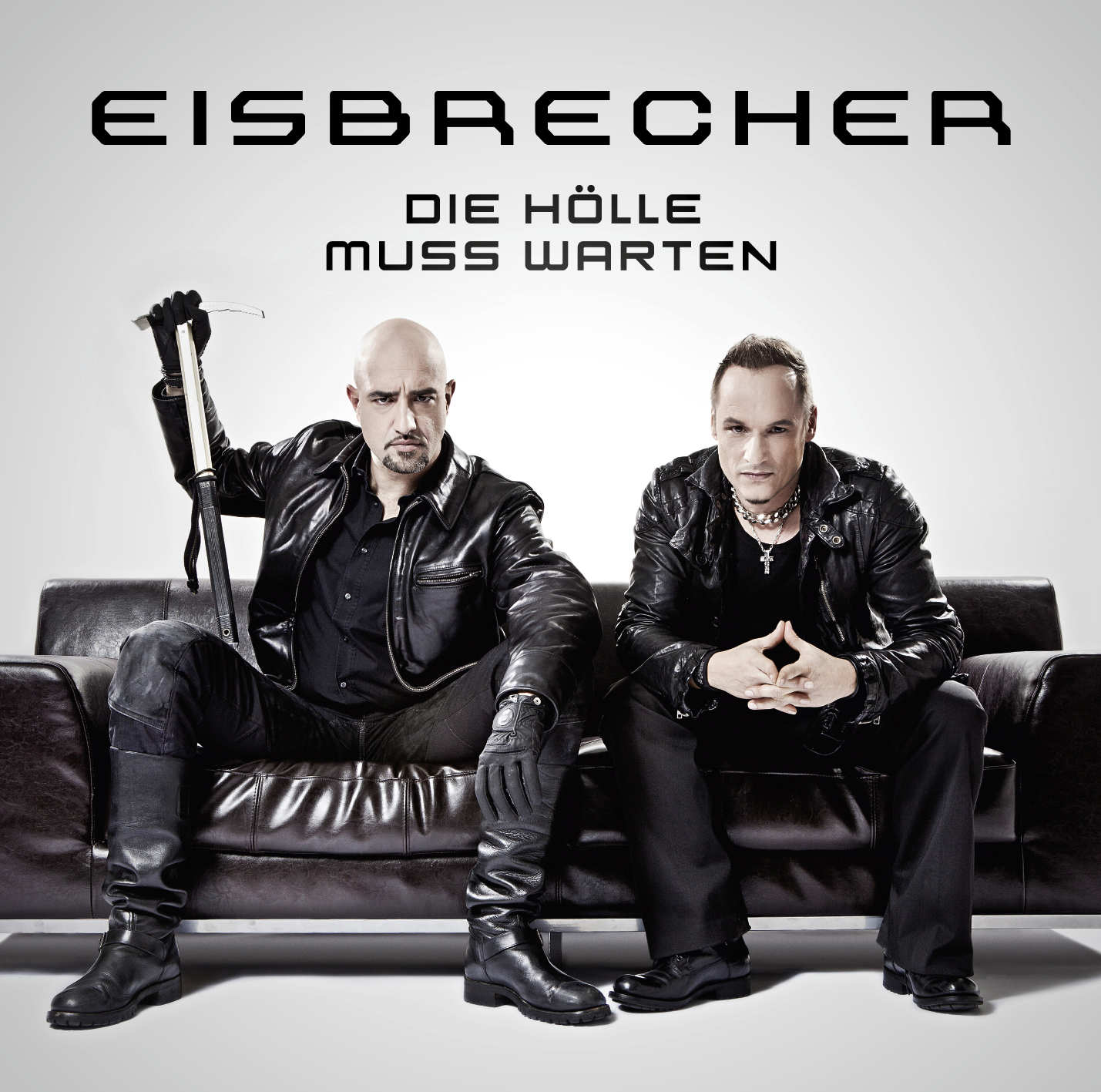 Zwei Männer auf einer Couch, einer hält eine Waffe, mit schwarzem Hintergrund.