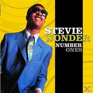 Stevie Wonder lächelt, trägt eine Sonnenbrille und einen blauen Anzug, gelb-schwarzer Hintergrund.