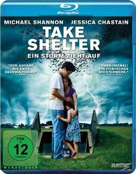 Filmplakat für 'Take Shelter'. Eine Familie umarmt sich unter Gewitterwolken. Blaues und schwarzes Farbschema.
